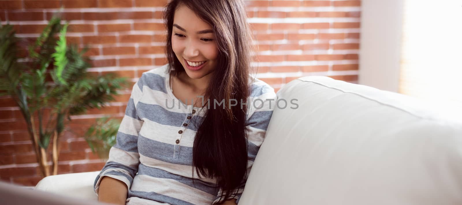 Smiling asian woman using laptop on couch at home in the living room