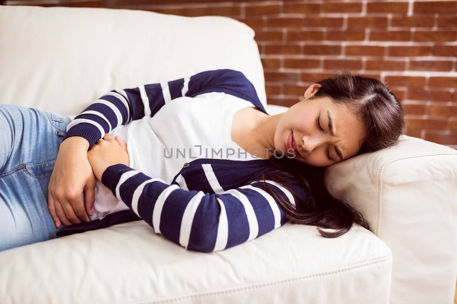 Asian woman lying on the couch with cramps by Wavebreakmedia
