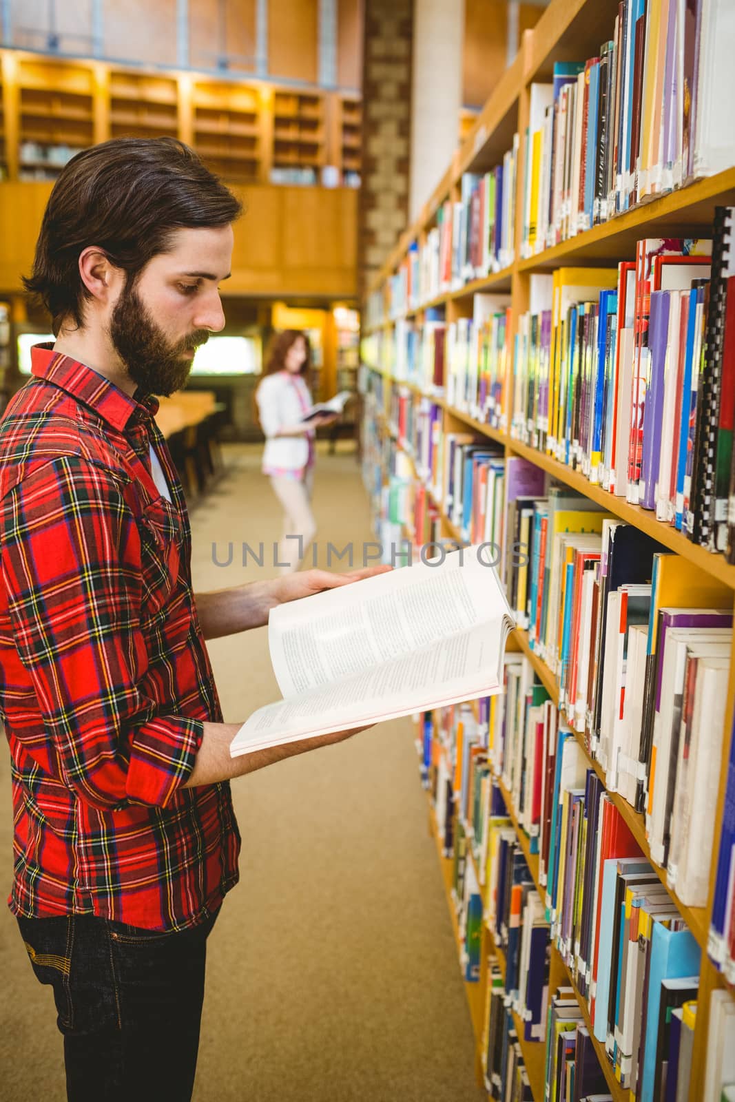 Hipster student picking a book in library by Wavebreakmedia