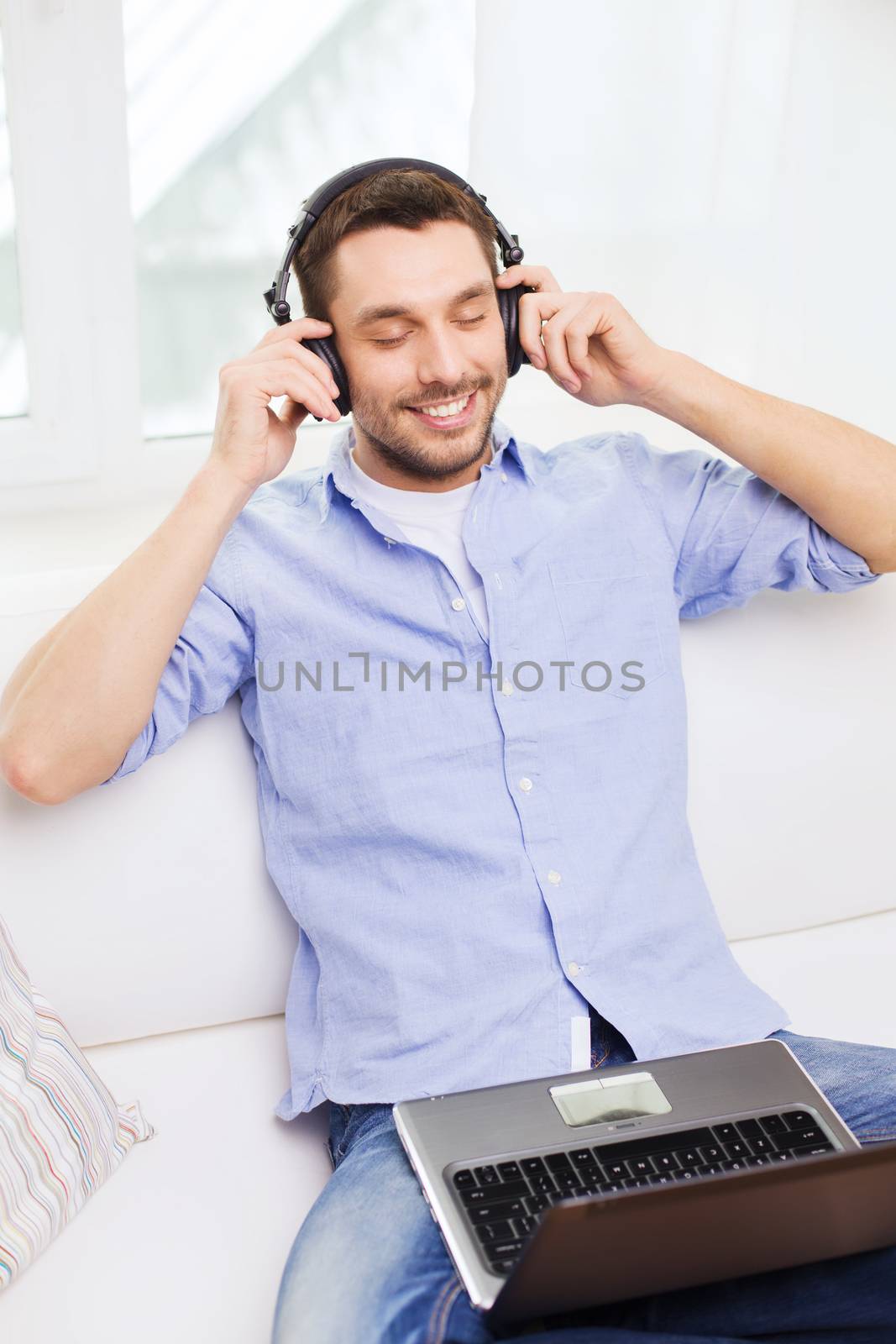 smiling man with laptop and headphones at home by dolgachov