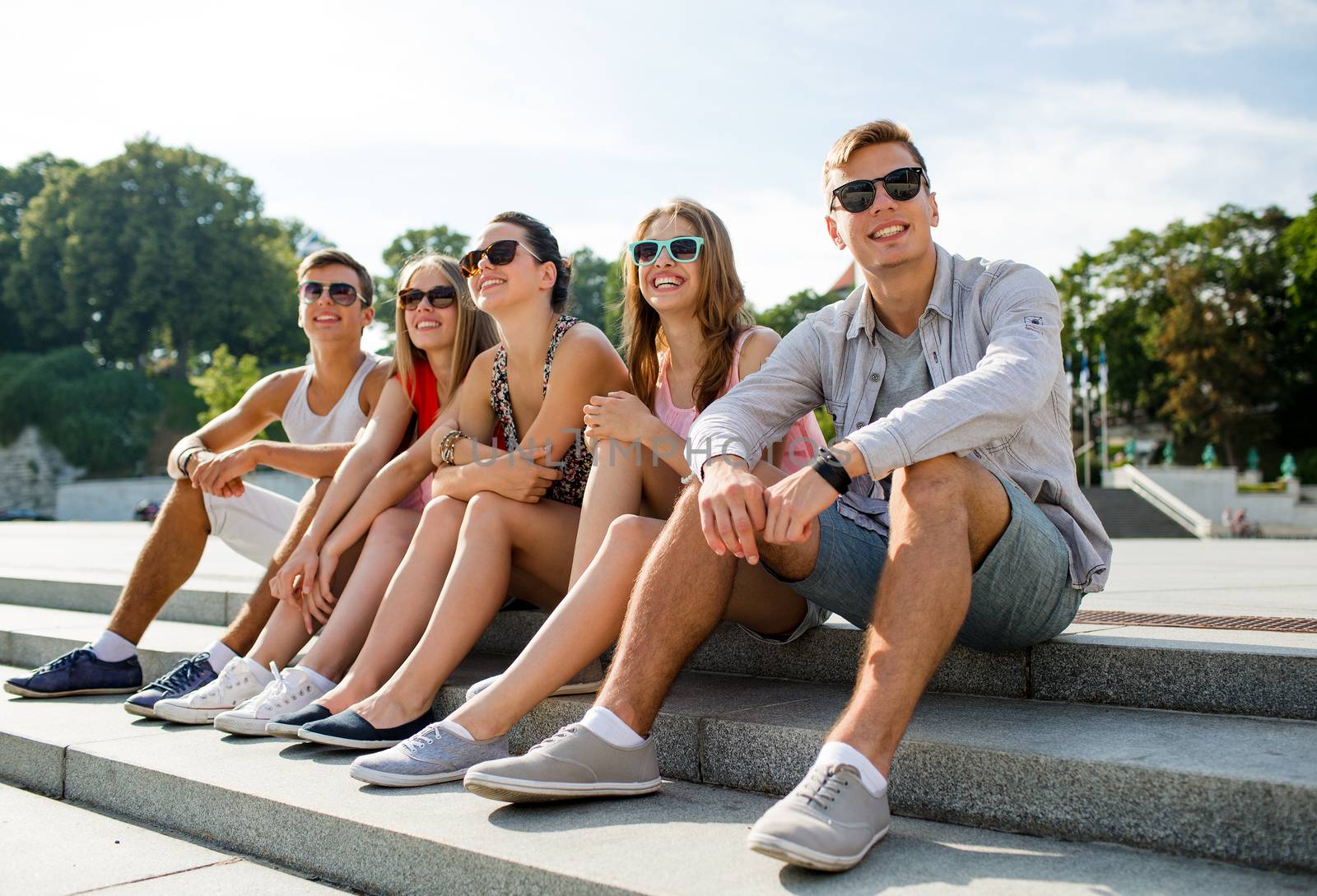 friendship, leisure, summer and people concept - group of smiling friends sitting on city street