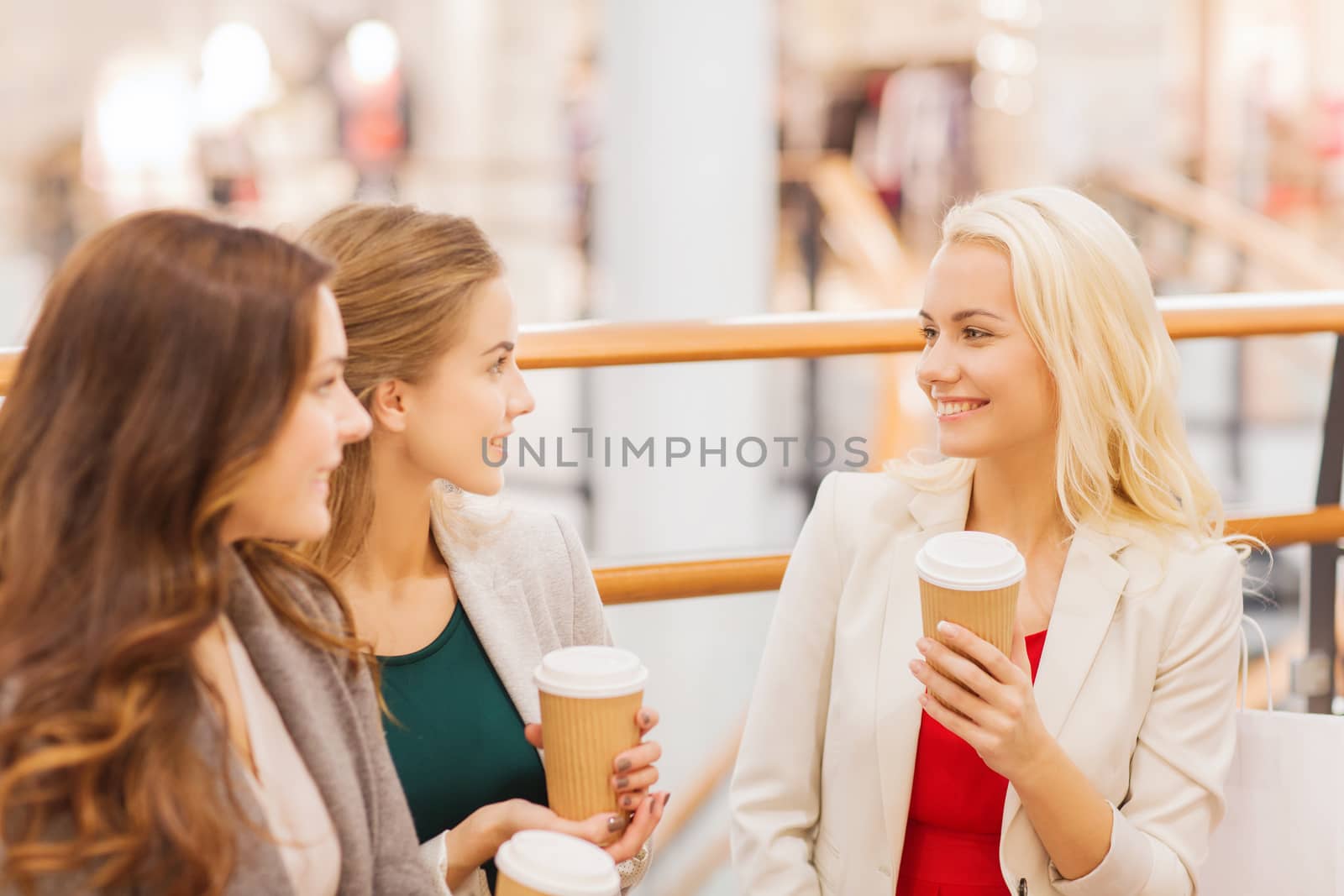 sale, consumerism and people concept - happy young women with shopping bags and coffee paper cups in mall