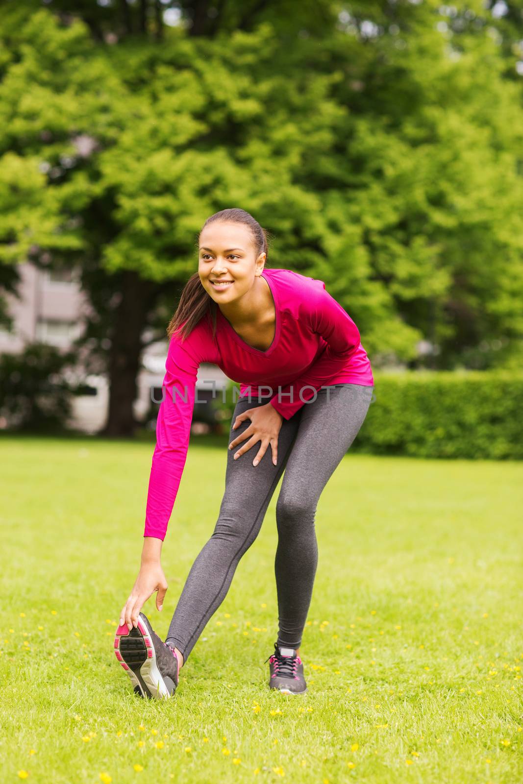 fitness, sport, training, park and lifestyle concept - smiling woman stretching leg outdoors