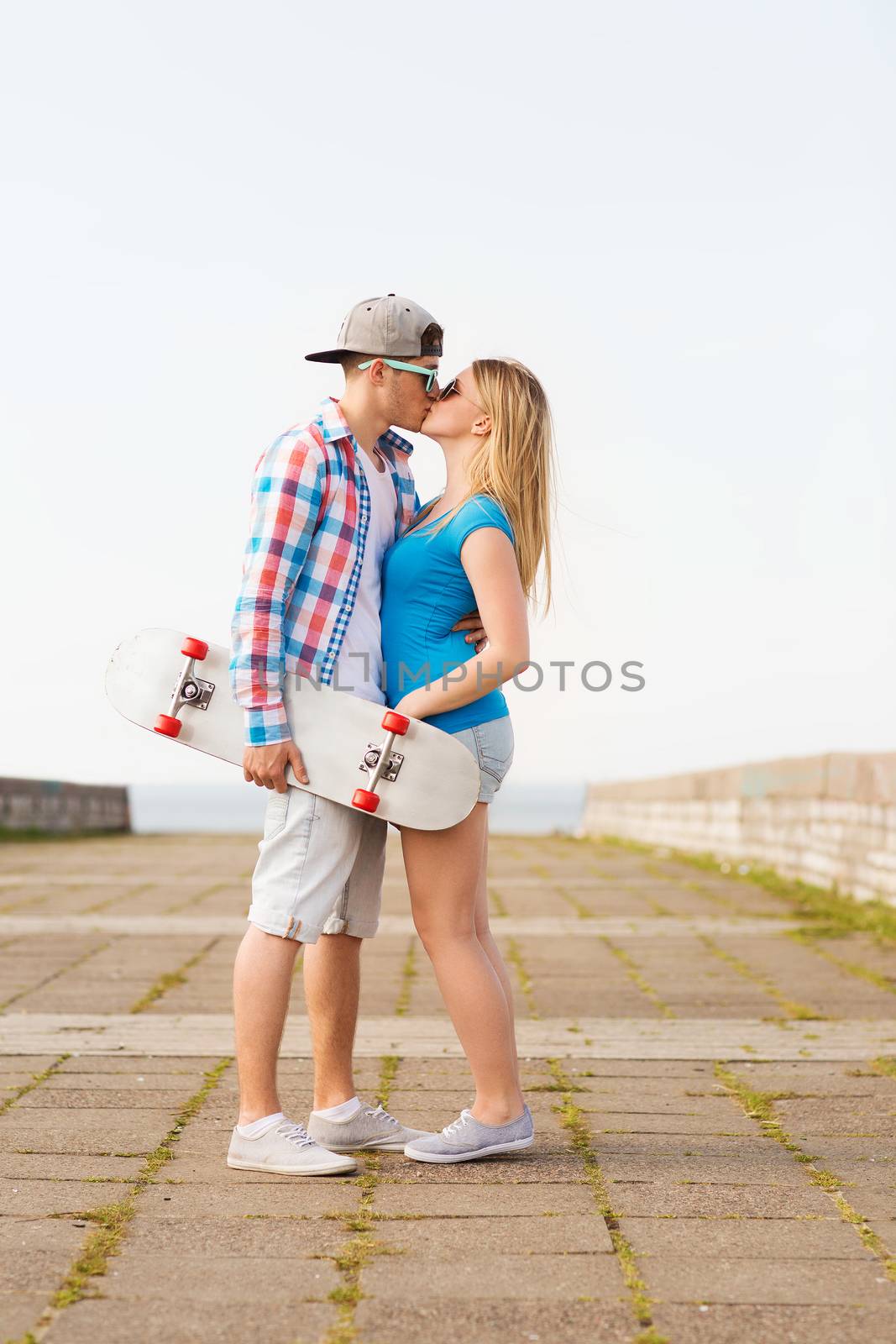 holidays, vacation, love and friendship concept - smiling couple with skateboard kissing outdoors