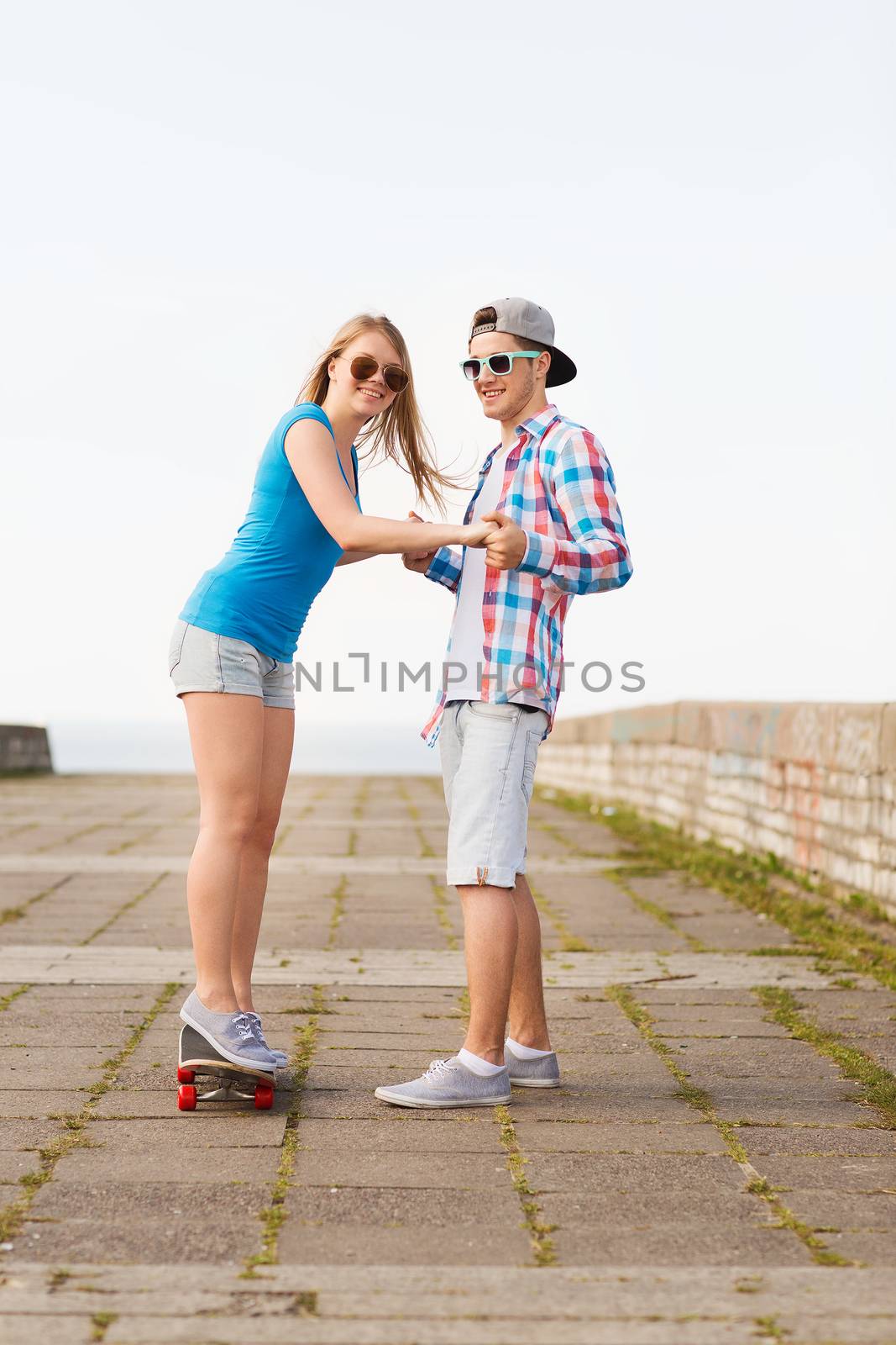 smiling couple with skateboard outdoors by dolgachov