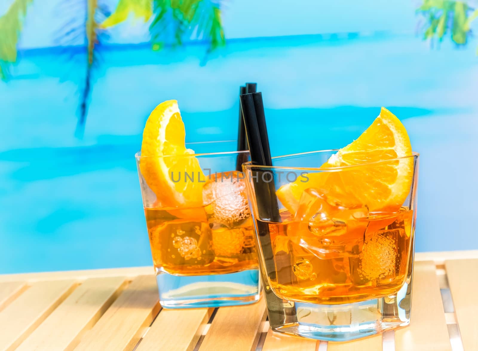 two glasses of spritz aperitif aperol cocktail with orange slices and ice cubes on blur beach and palm background, summer concept