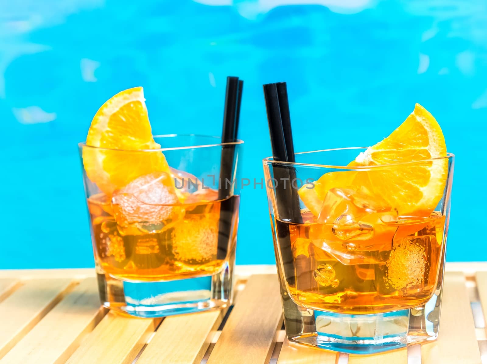 two glasses of spritz aperitif aperol cocktail with orange slices and ice cubes on swimming pool background, summer concept