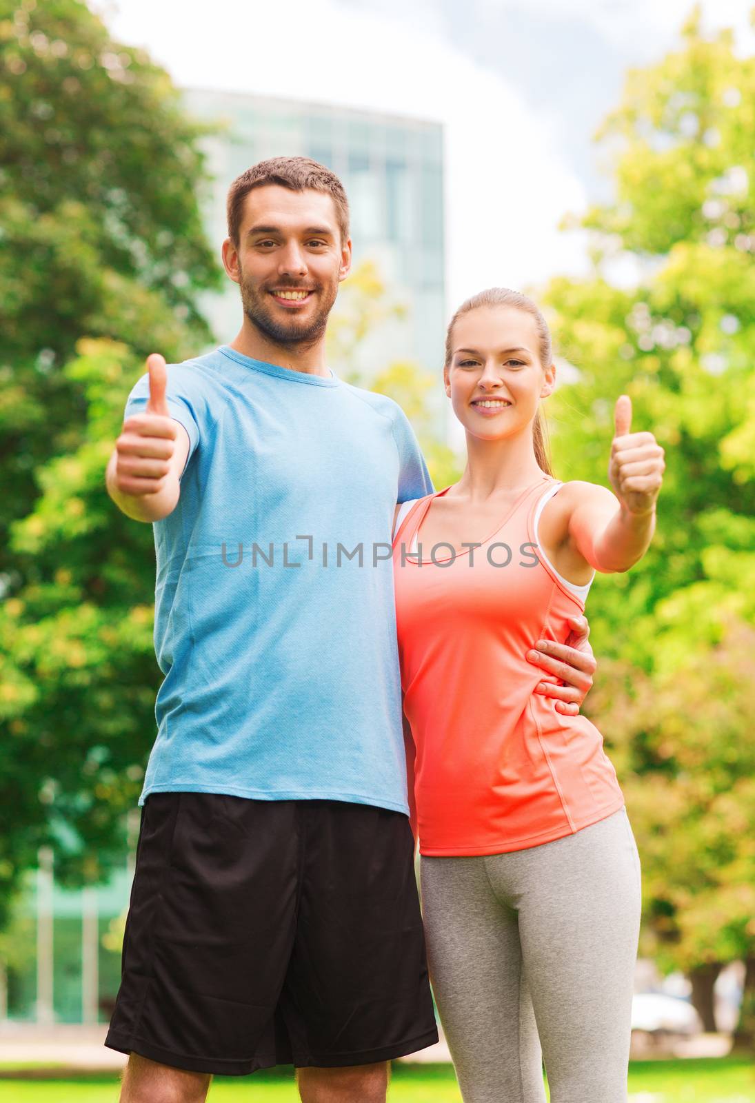 fitness, sport, friendship and lifestyle concept - smiling couple outdoors showing thumbs up