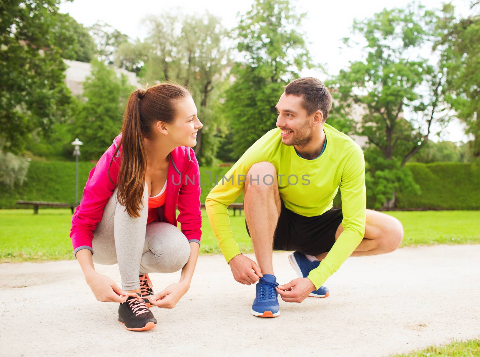 fitness, sport, friendship and lifestyle concept - smiling couple tying shoelaces outdoors