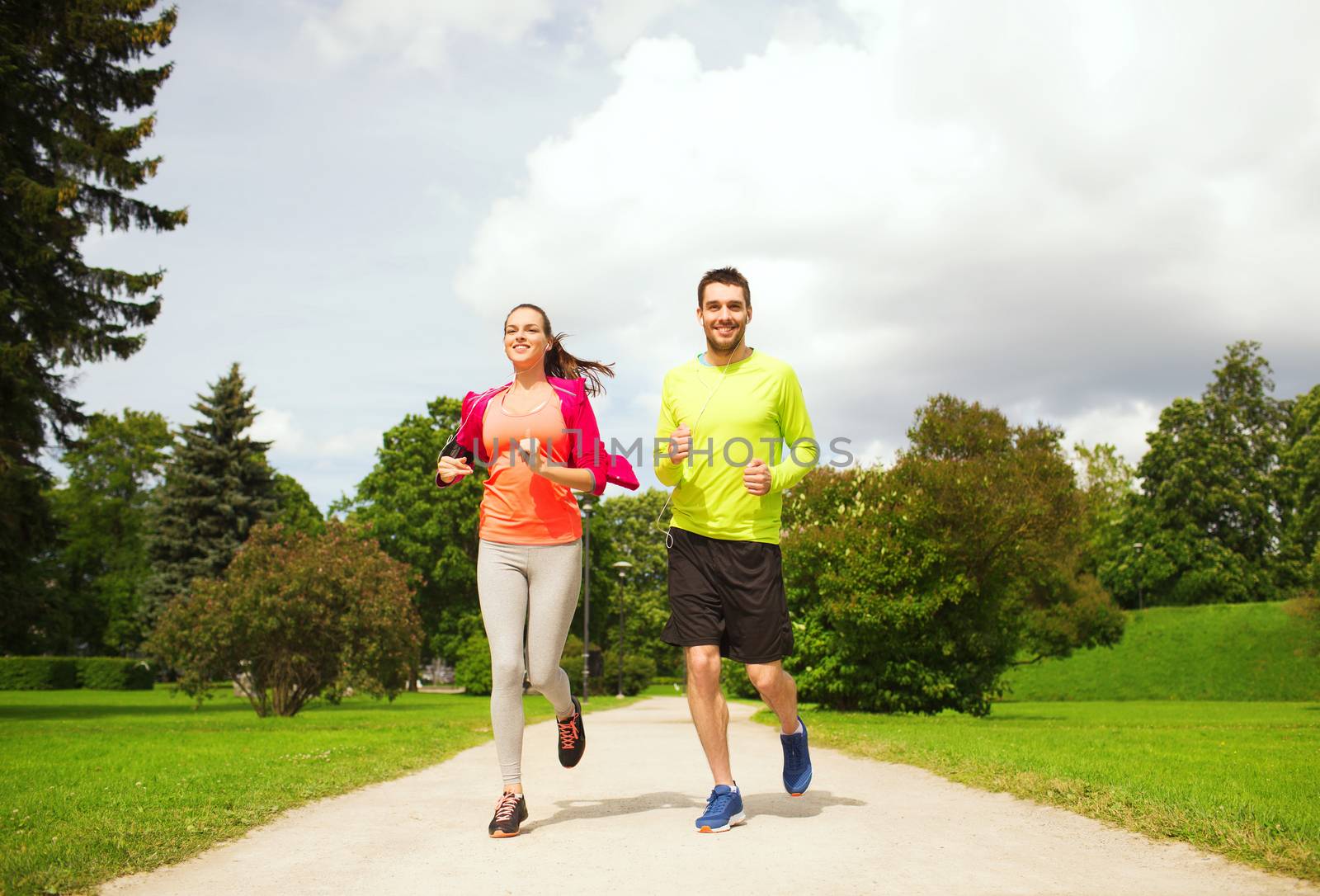 fitness, sport, friendship and lifestyle concept - smiling couple with earphones running outdoors