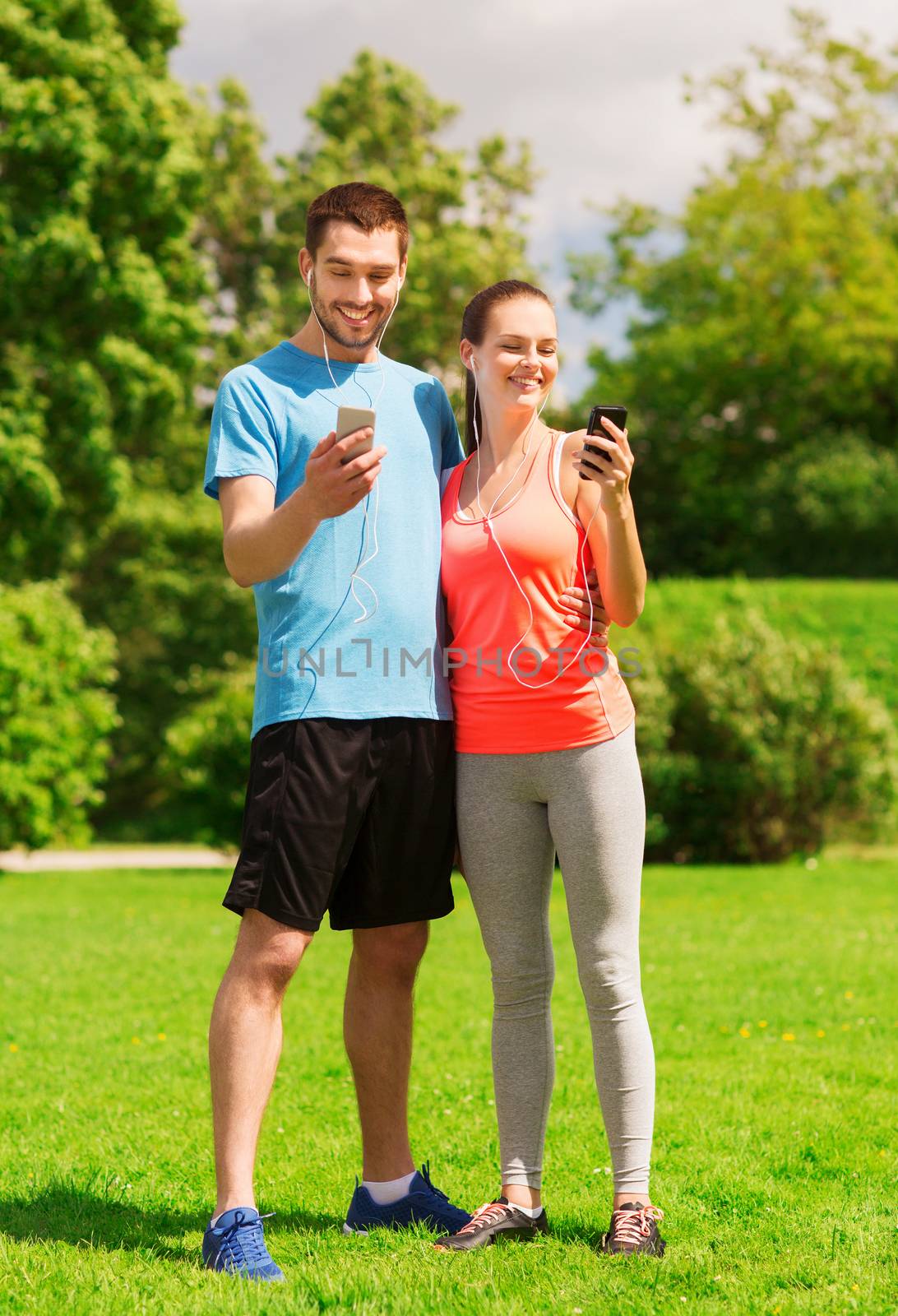 two smiling people with smartphones outdoors by dolgachov