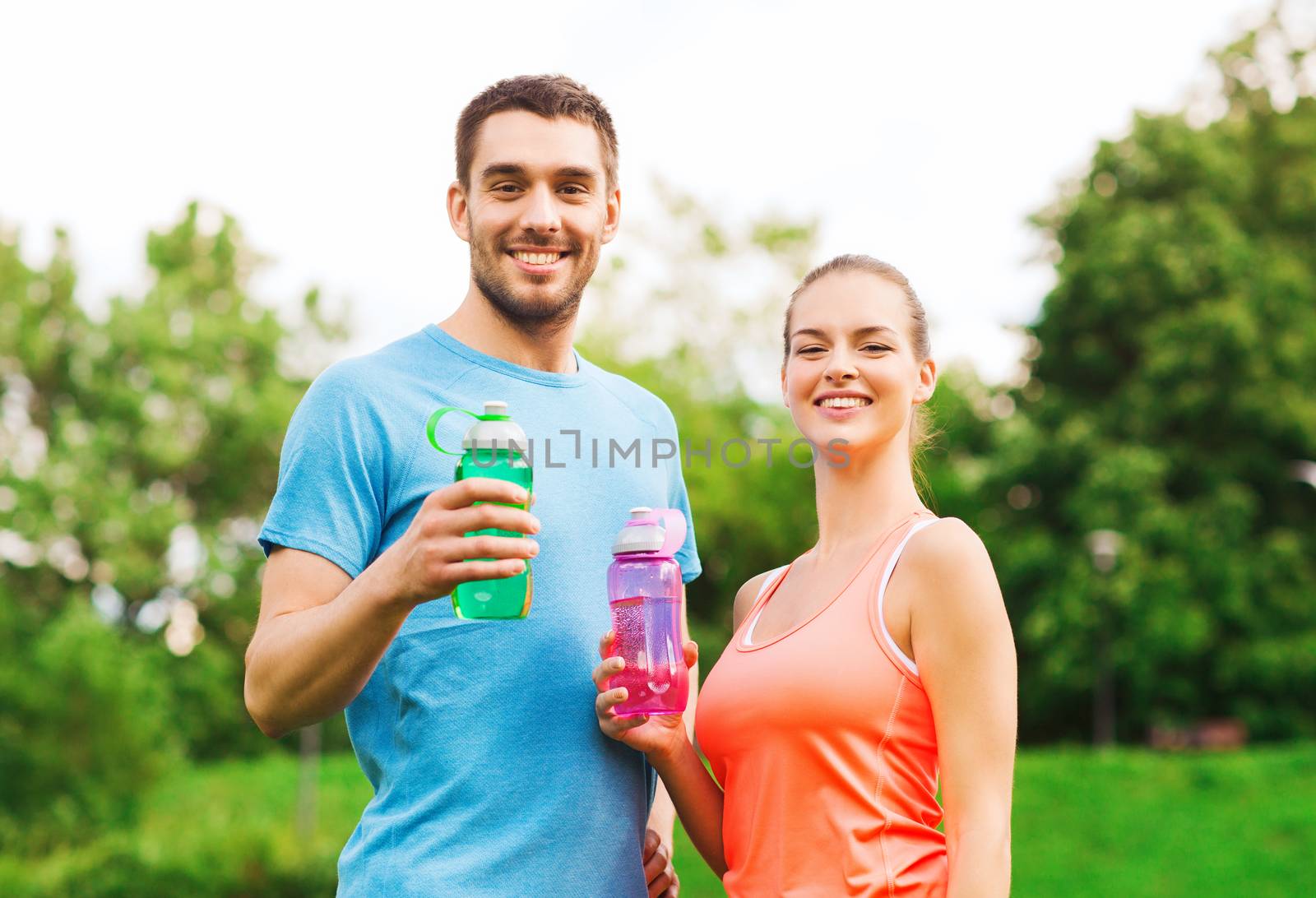 fitness, sport, friendship and lifestyle concept - smiling couple with bottles of water outdoors