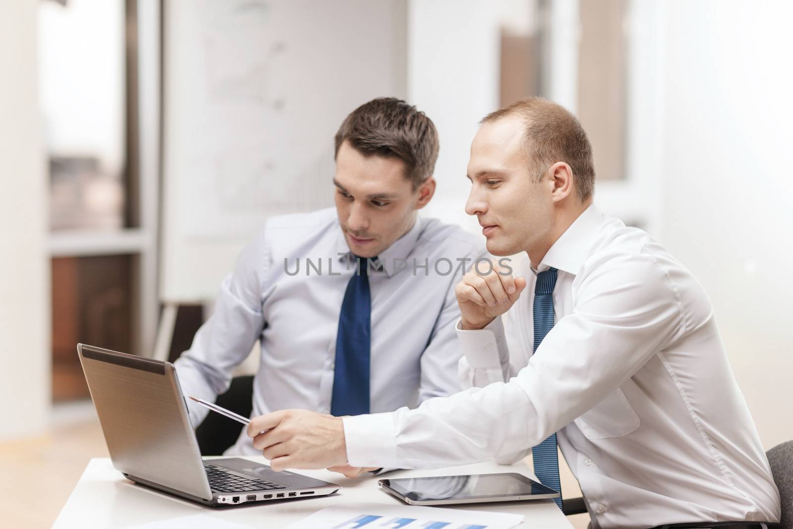 business, technology and office concept - two businessmen with laptop, tablet pc computer and papers having discussion in office