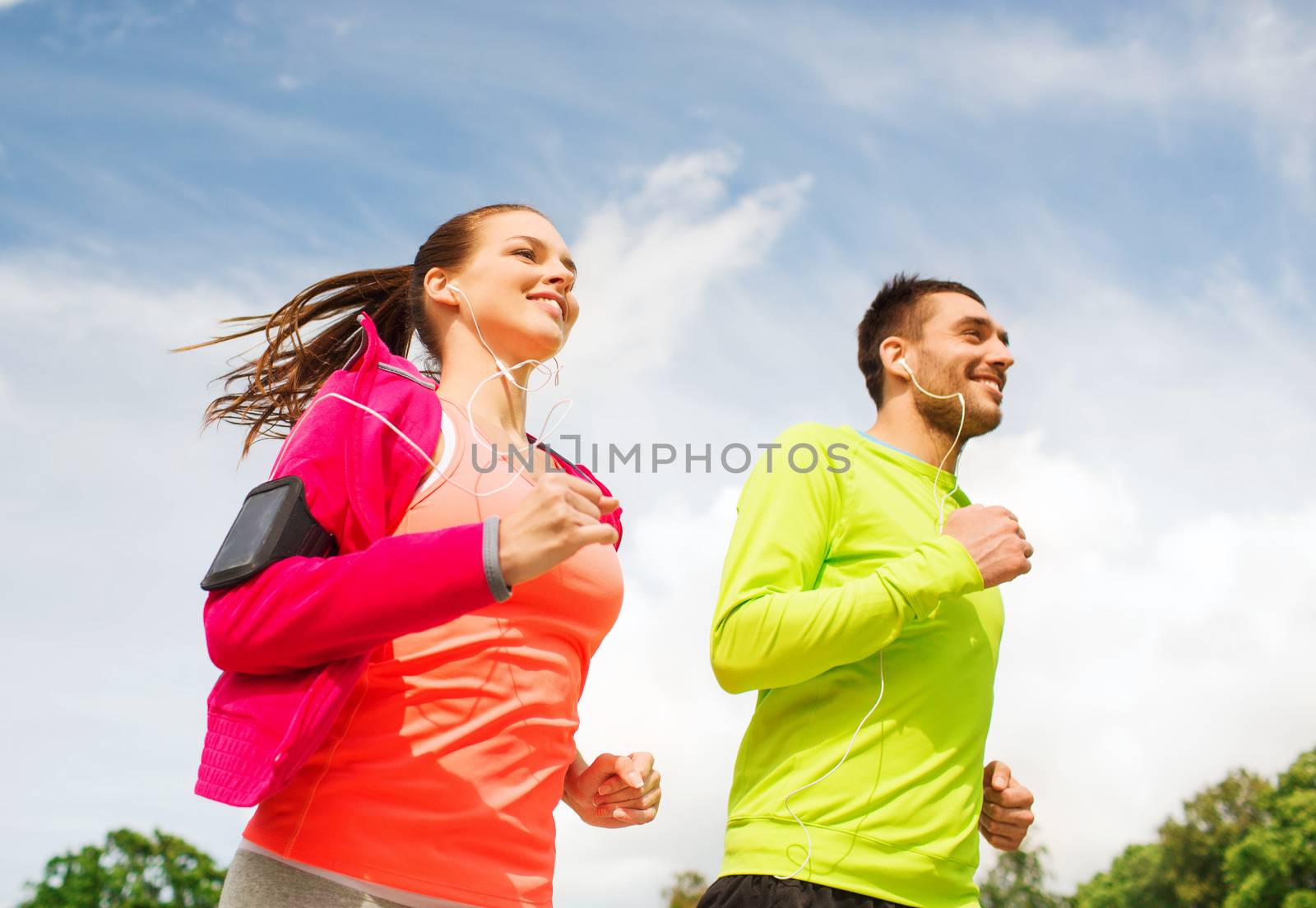 fitness, sport, friendship and lifestyle concept - smiling couple with earphones running outdoors