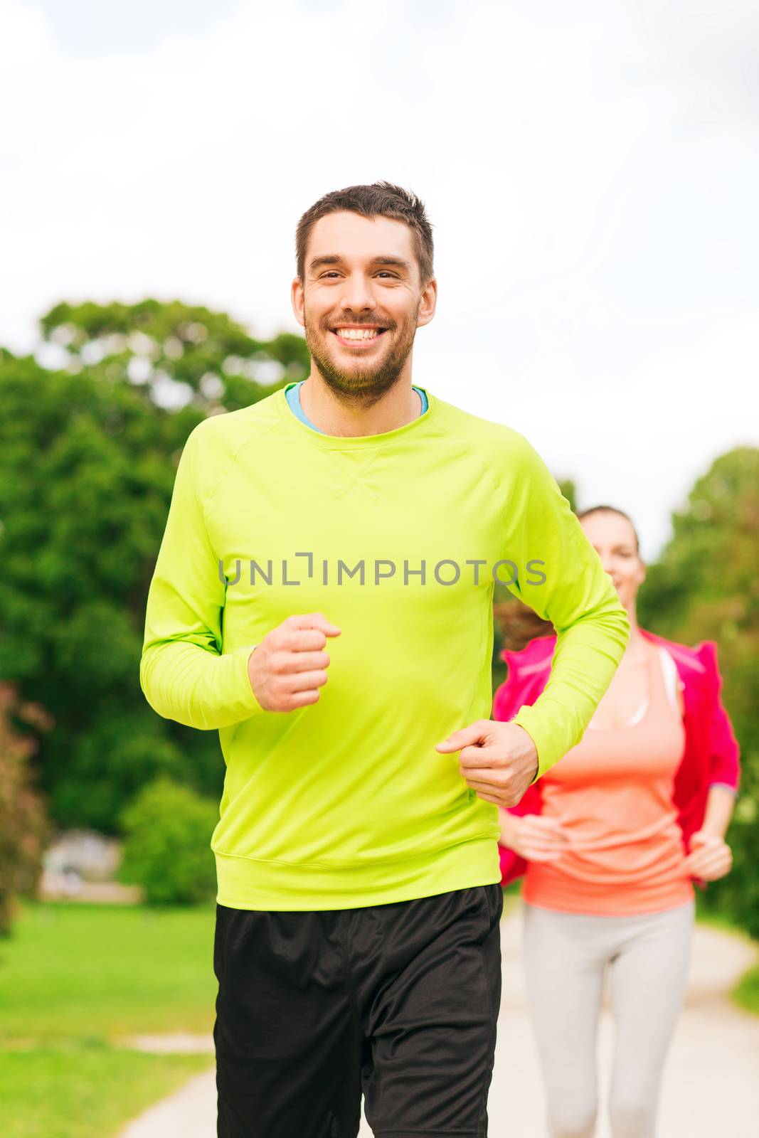 fitness, sport, friendship and lifestyle concept - smiling couple running outdoors