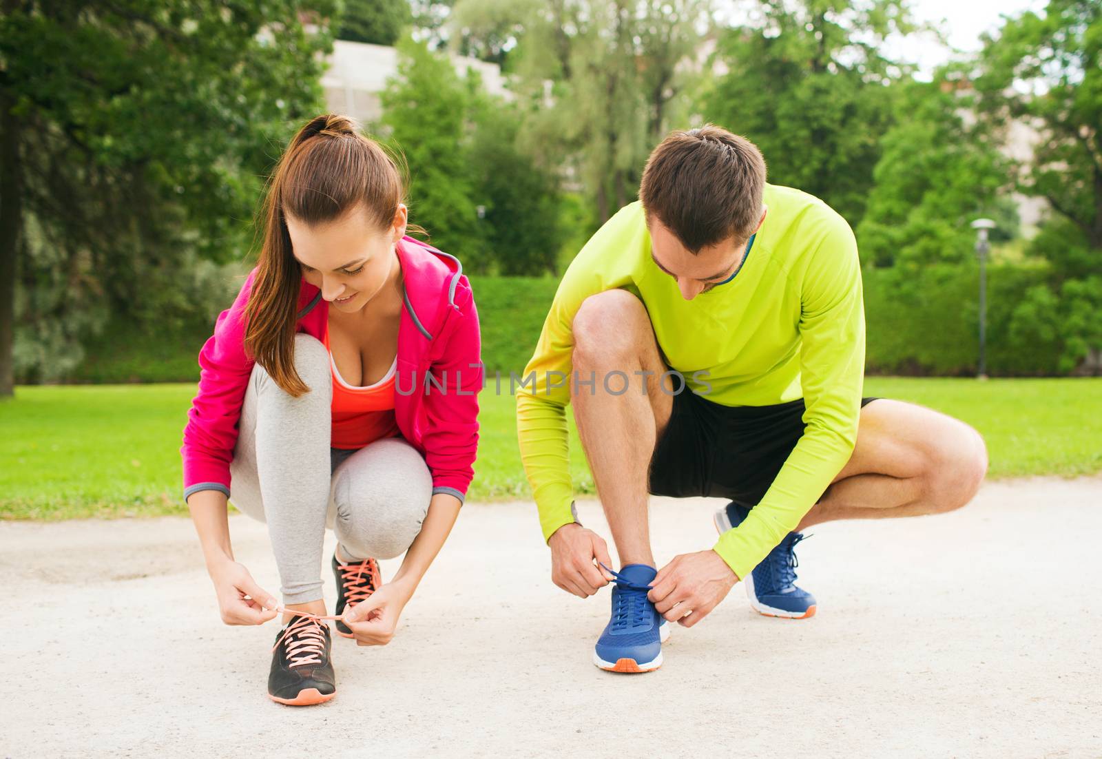 smiling couple tying shoelaces outdoors by dolgachov