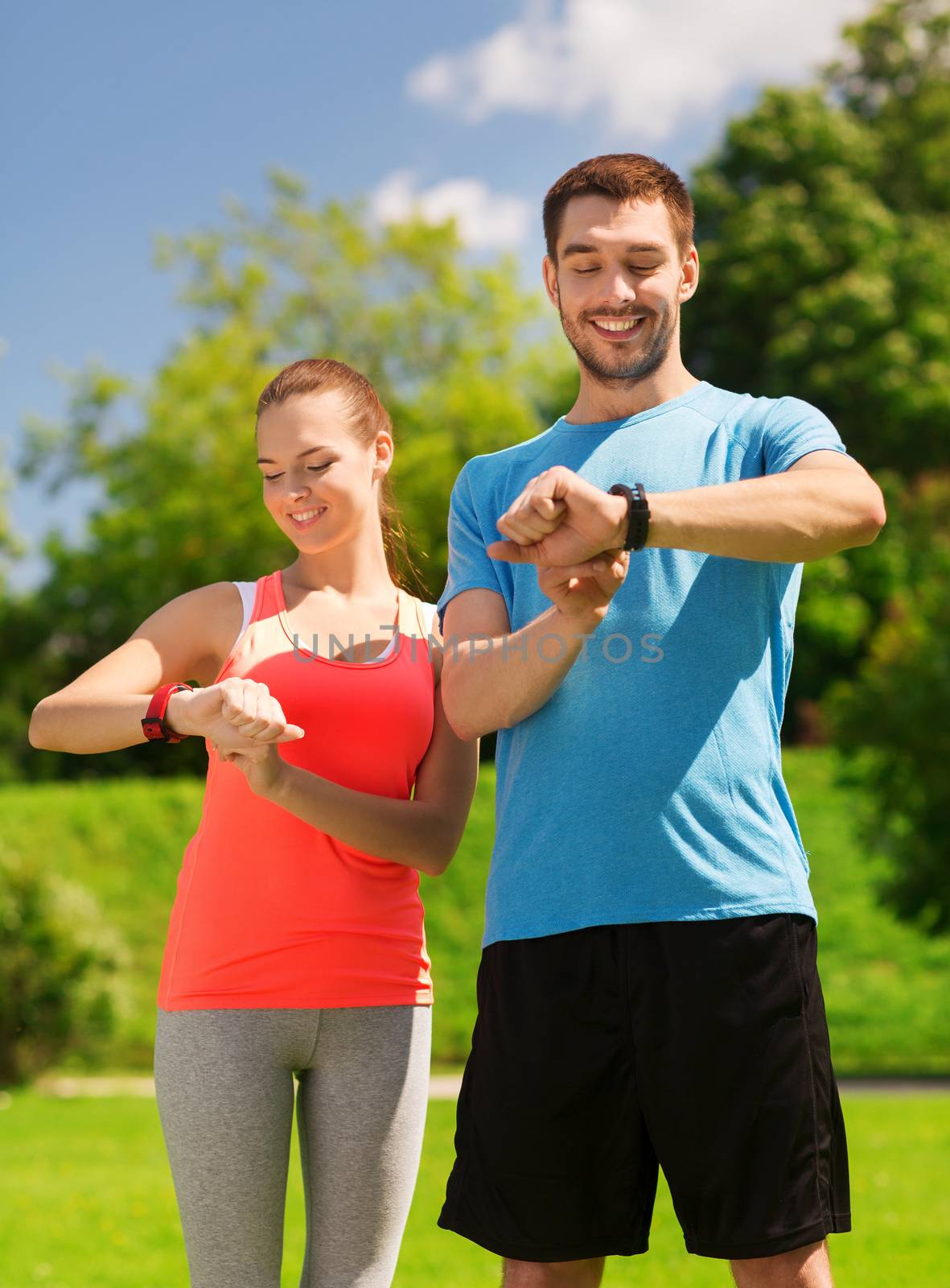 fitness, sport, training, technology and lifestyle concept - two smiling people with heart rate watches outdoors