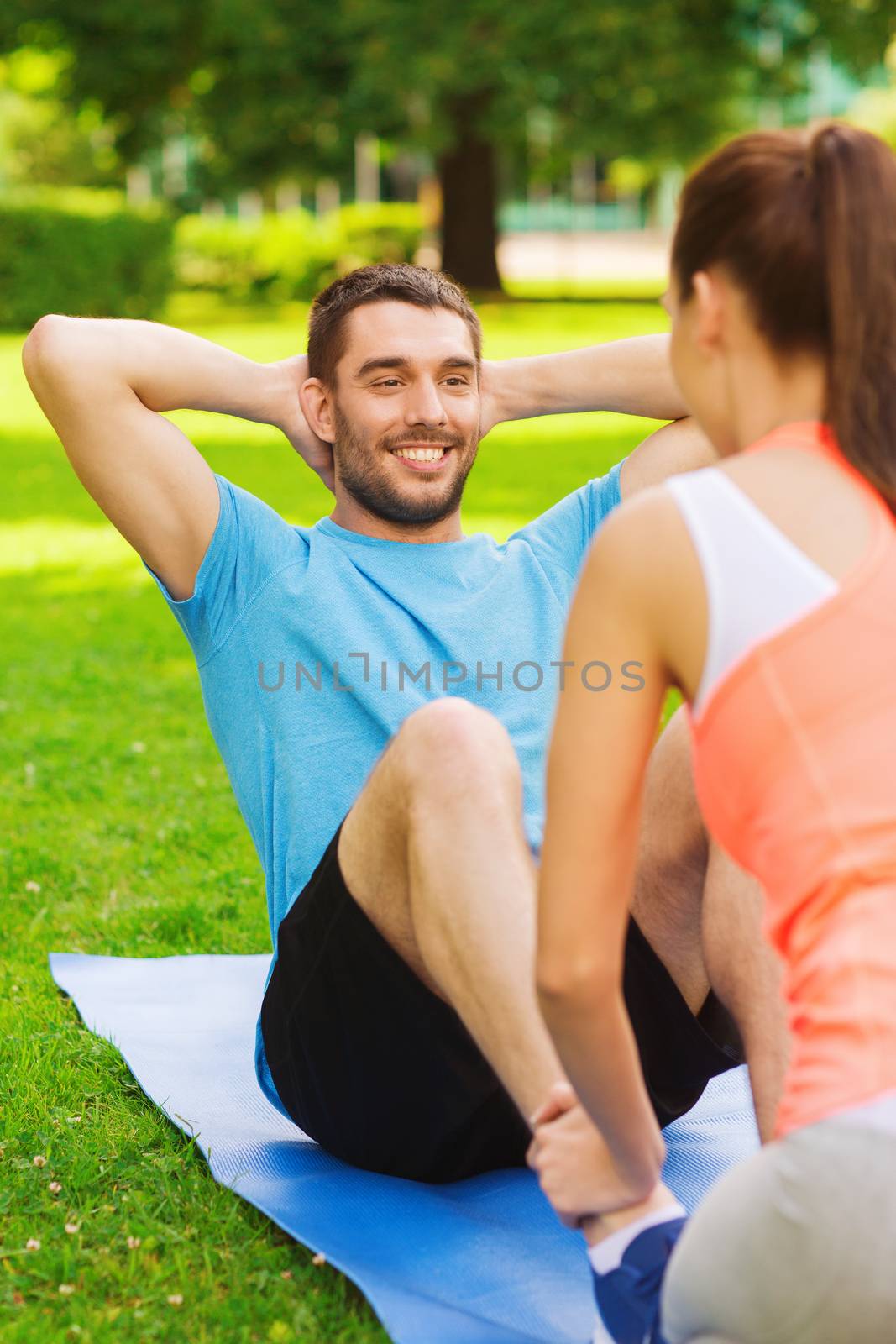 fitness, sport, training, teamwork and lifestyle concept - smiling man with personal trainer doing exercises on mat outdoors