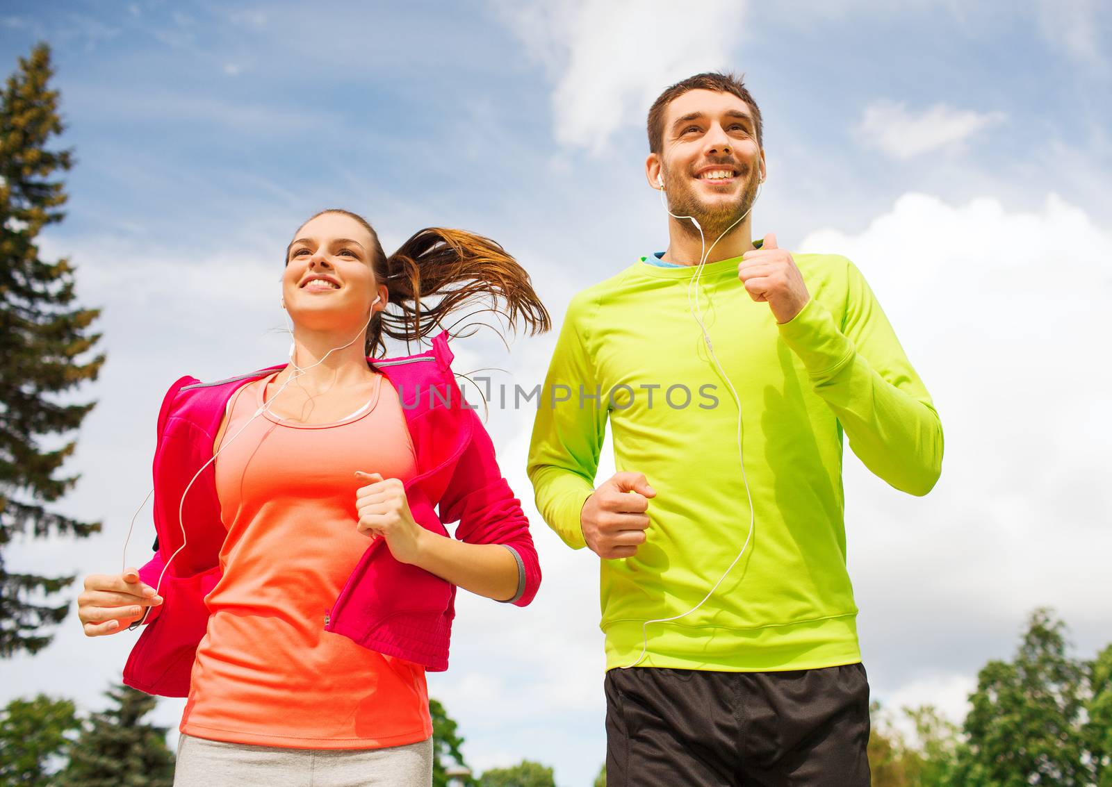 smiling couple with earphones running outdoors by dolgachov