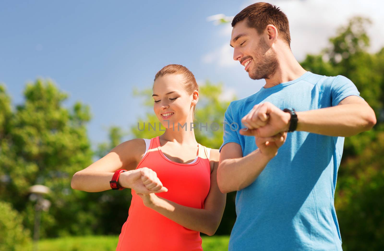 fitness, sport, training, technology and lifestyle concept - two smiling people with heart rate watches outdoors