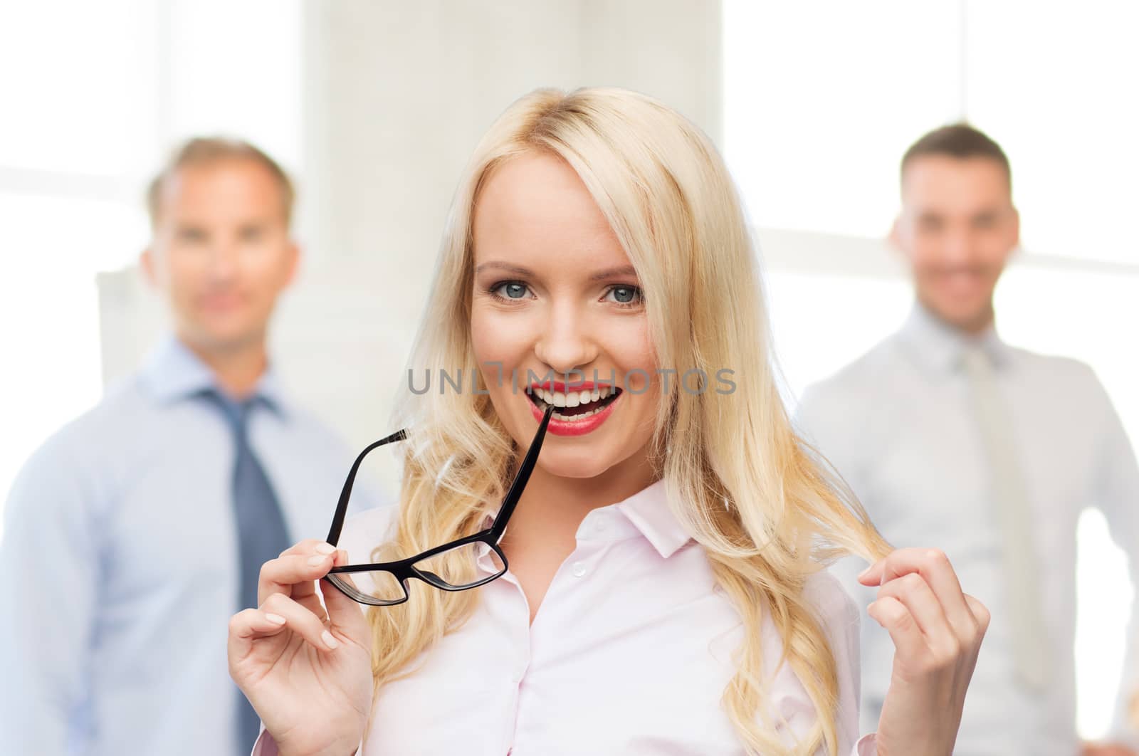 business, teamwork and people concept - smiling businesswoman, student or secretary with eyeglasses over office and group of colleagues background