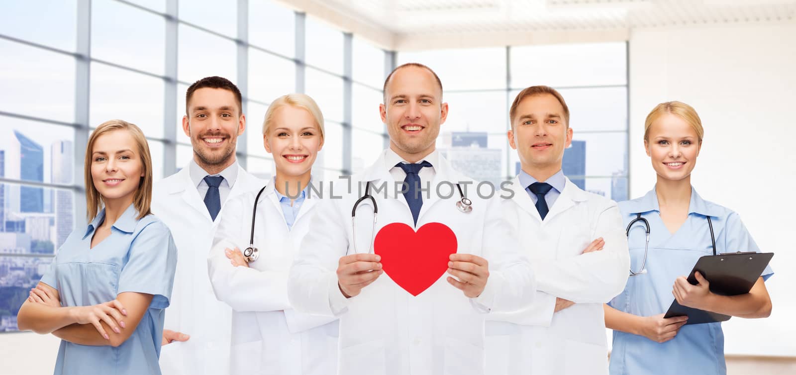 medicine, cardiology, healthcare and people concept - happy young doctors cardiologists with red heart over clinic background