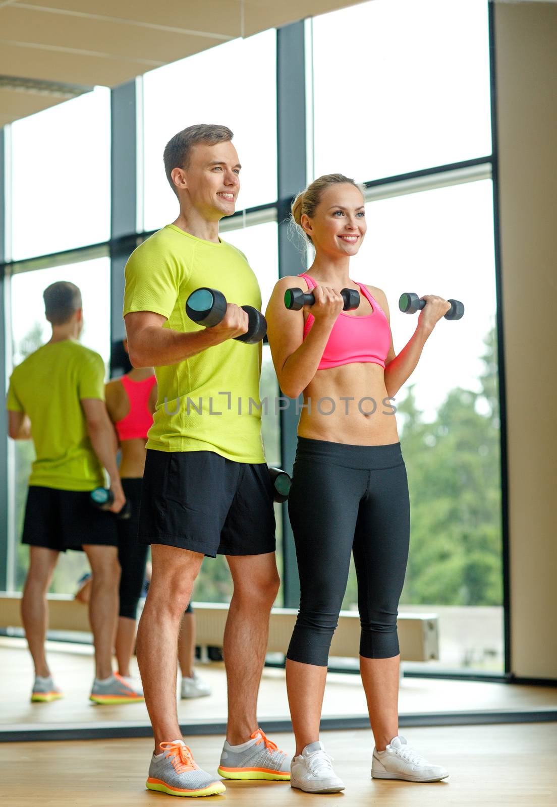 smiling man and woman with dumbbells in gym by dolgachov