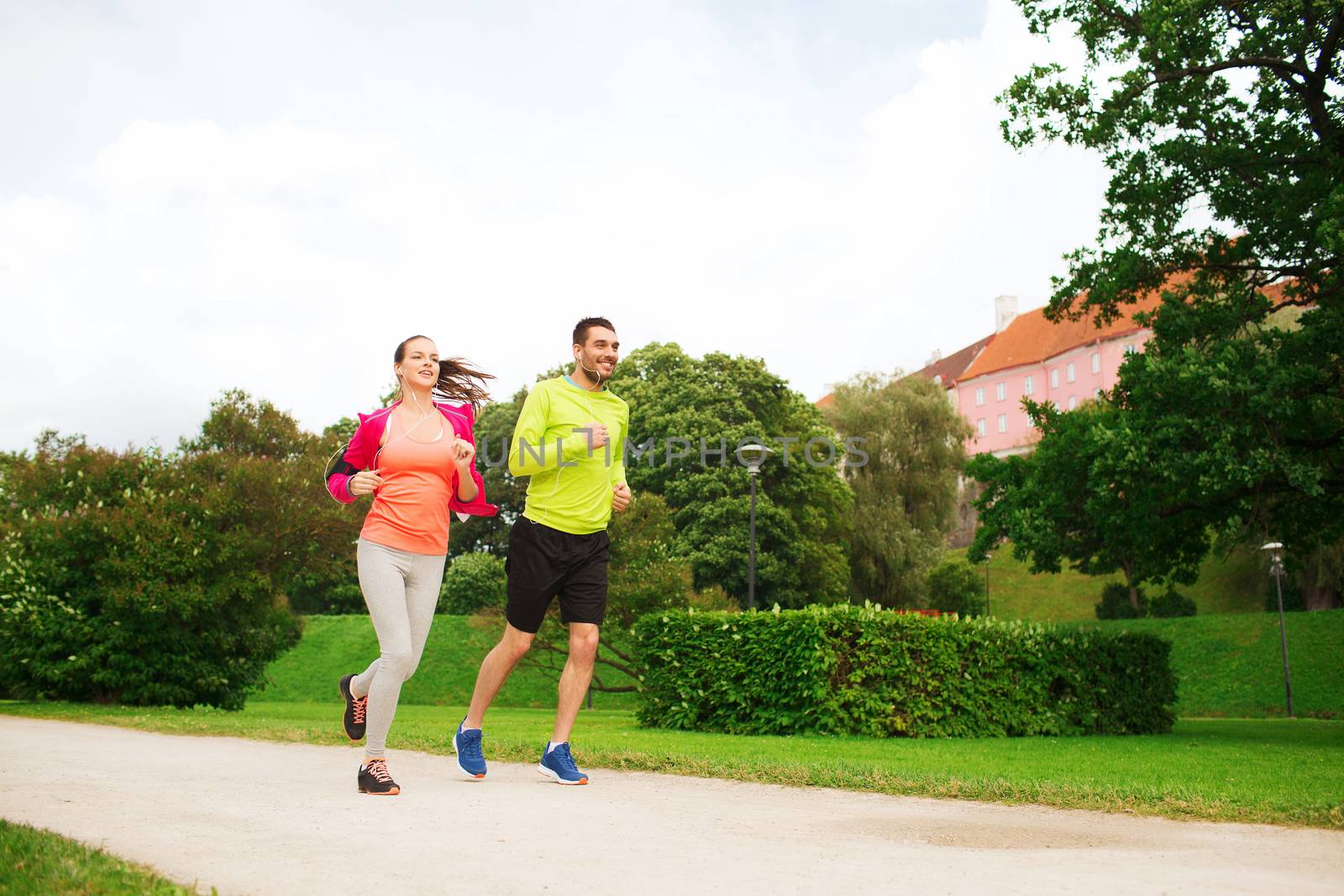 fitness, sport, friendship and lifestyle concept - smiling couple with earphones running outdoors