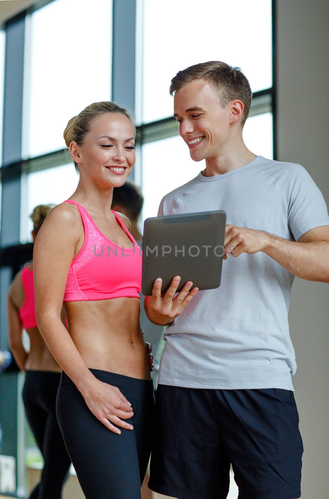 smiling young woman with personal trainer in gym by dolgachov