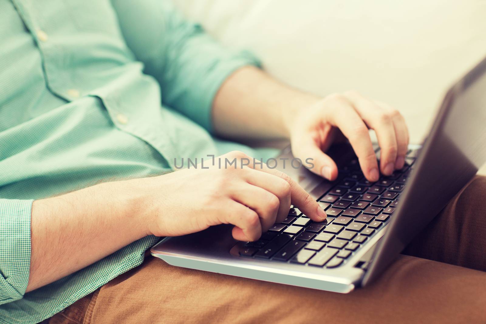 technology, home and lifestyle concept - close up of man working with laptop computer and sitting on sofa at home