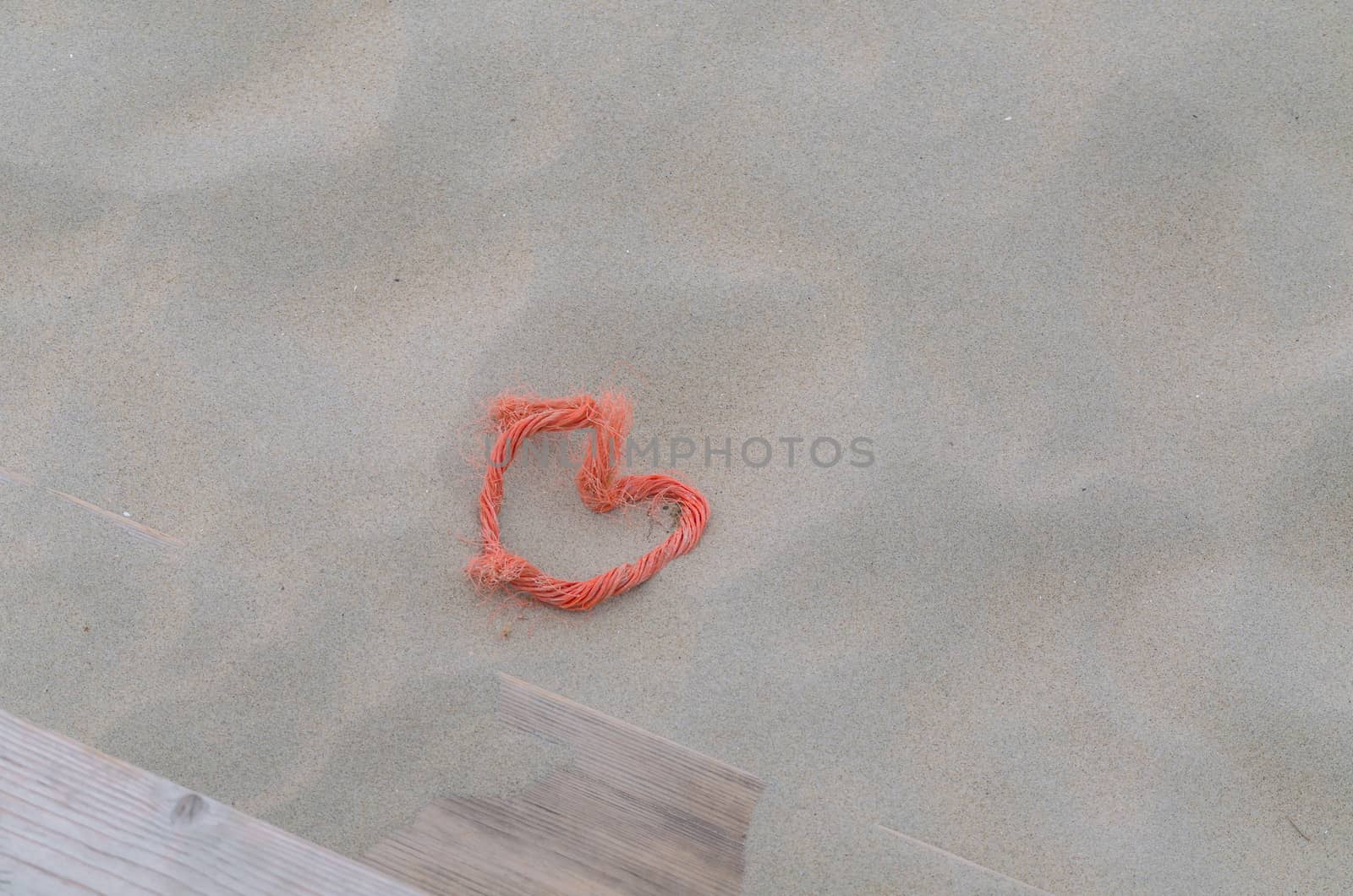 A red rope  in heart shape lying in the sand. Beach background. Top View