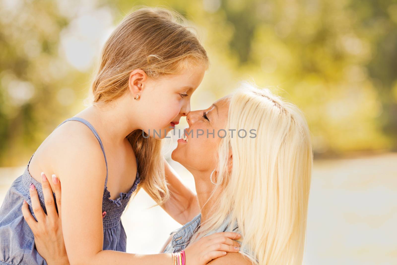 Beautiful, happy mother and daughter touching noses in the nature