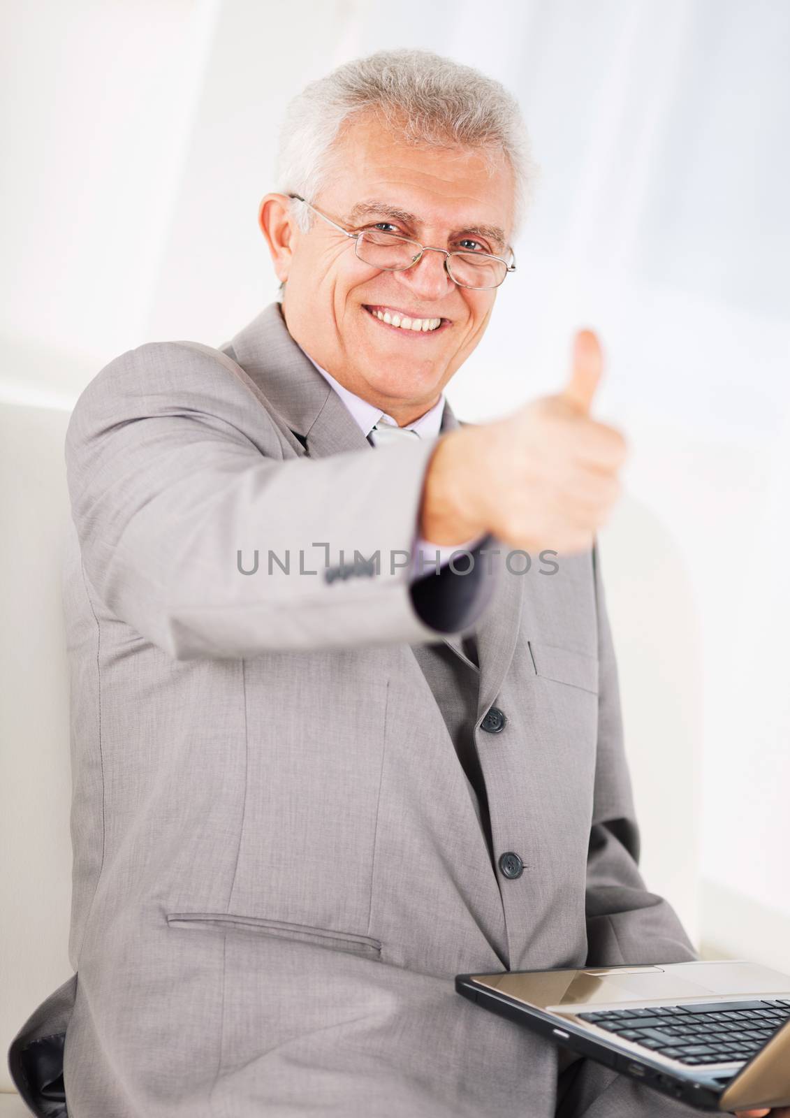 Happy Senior businessman working on laptop and showing thumbs up.