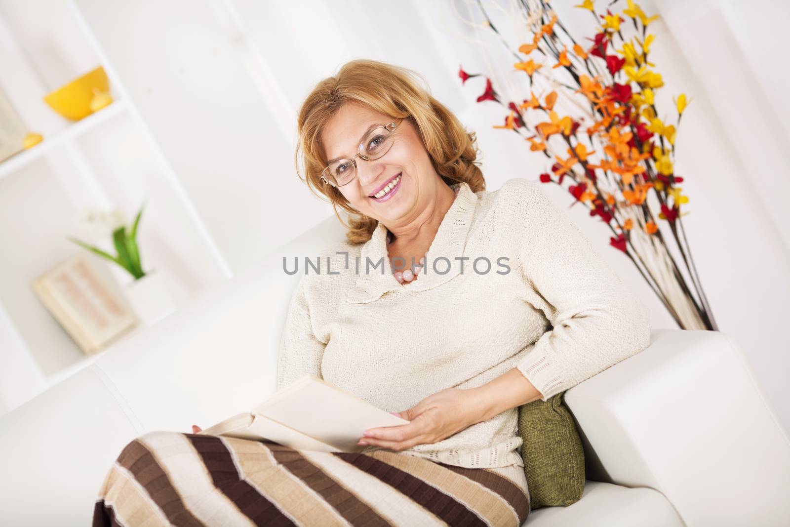 Senior woman sitting in living room and reading book.