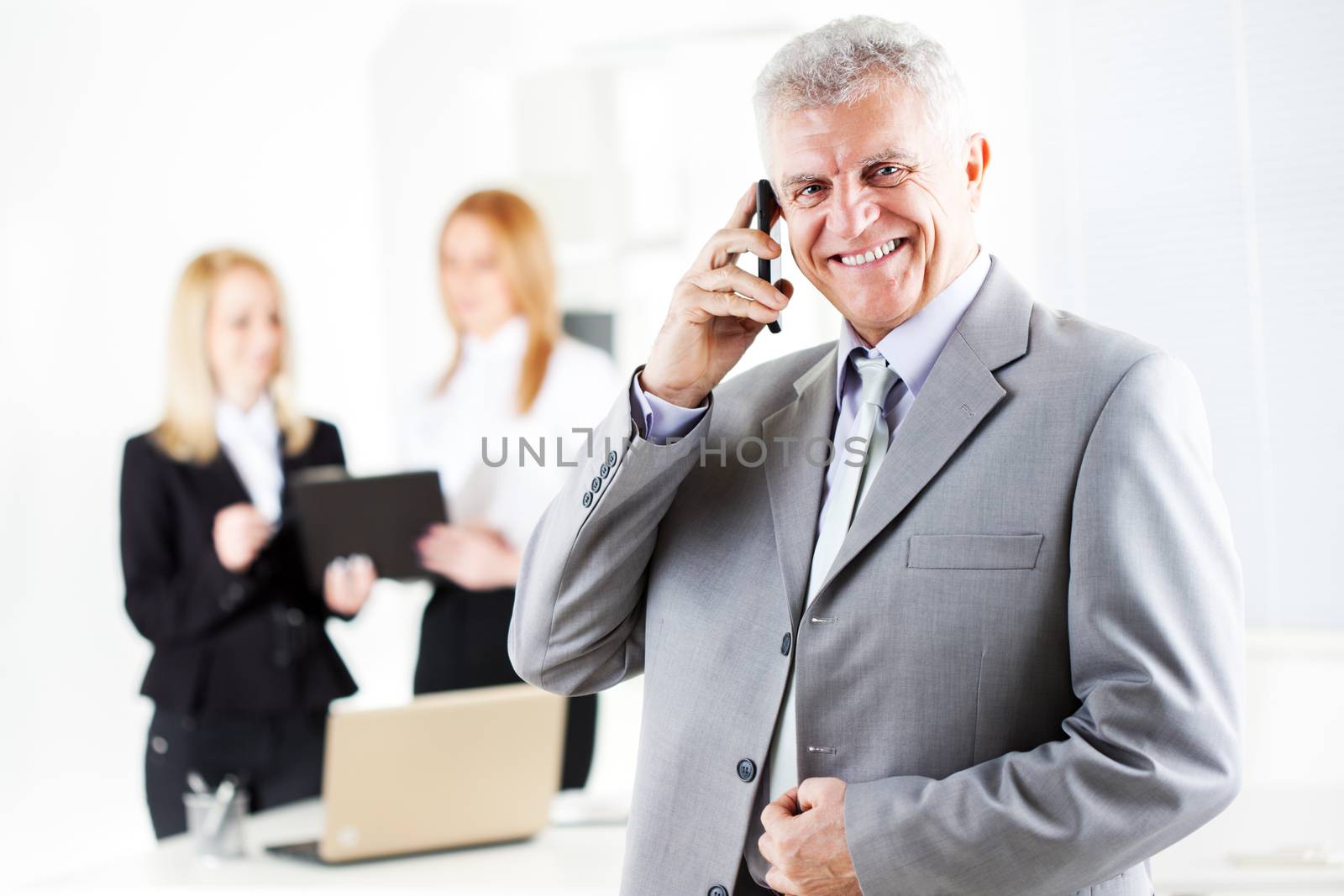 Happy senior businessman talking on mobile phone in the office. Looking at camera. Selective Focus.