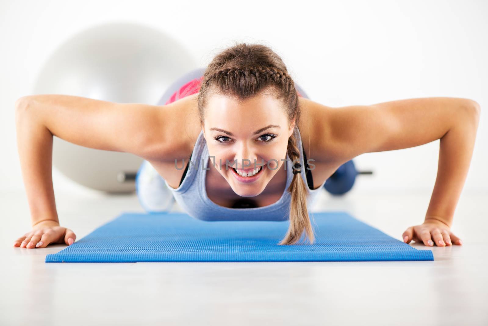 Young beautiful girl doing push-ups on exercise mat.  Looking At Camera.