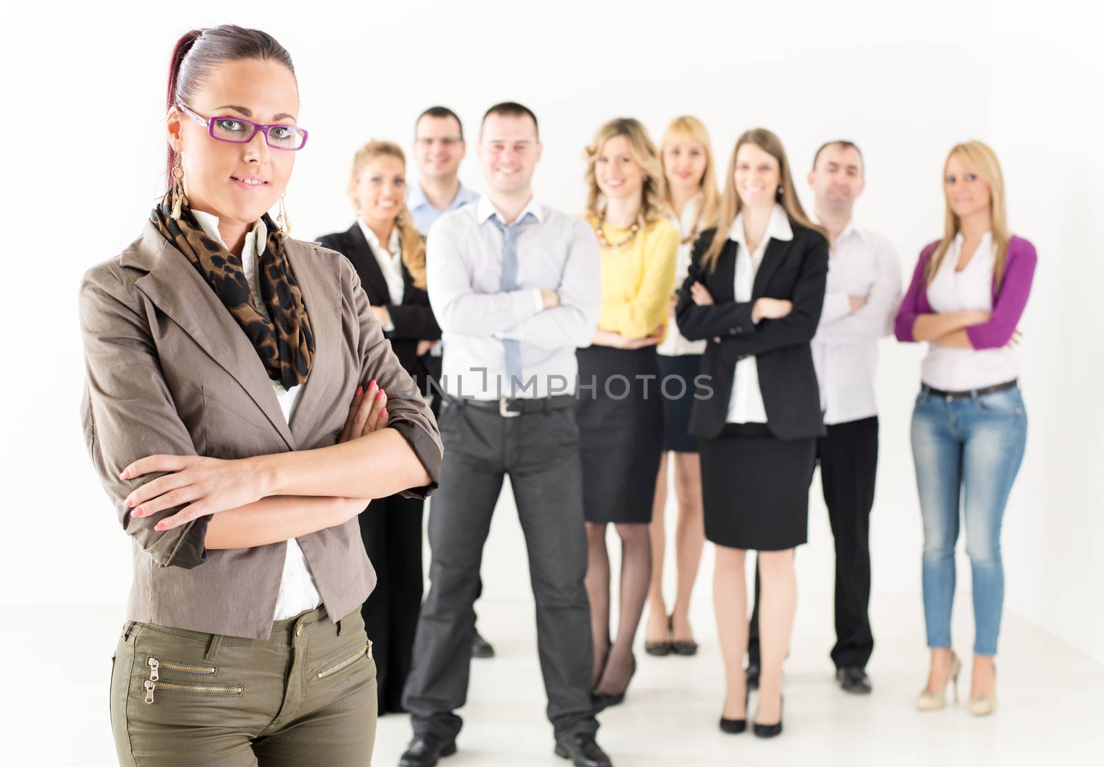 Smiling businesswoman standing in front of colleagues with crossed arm and looking at the camera.