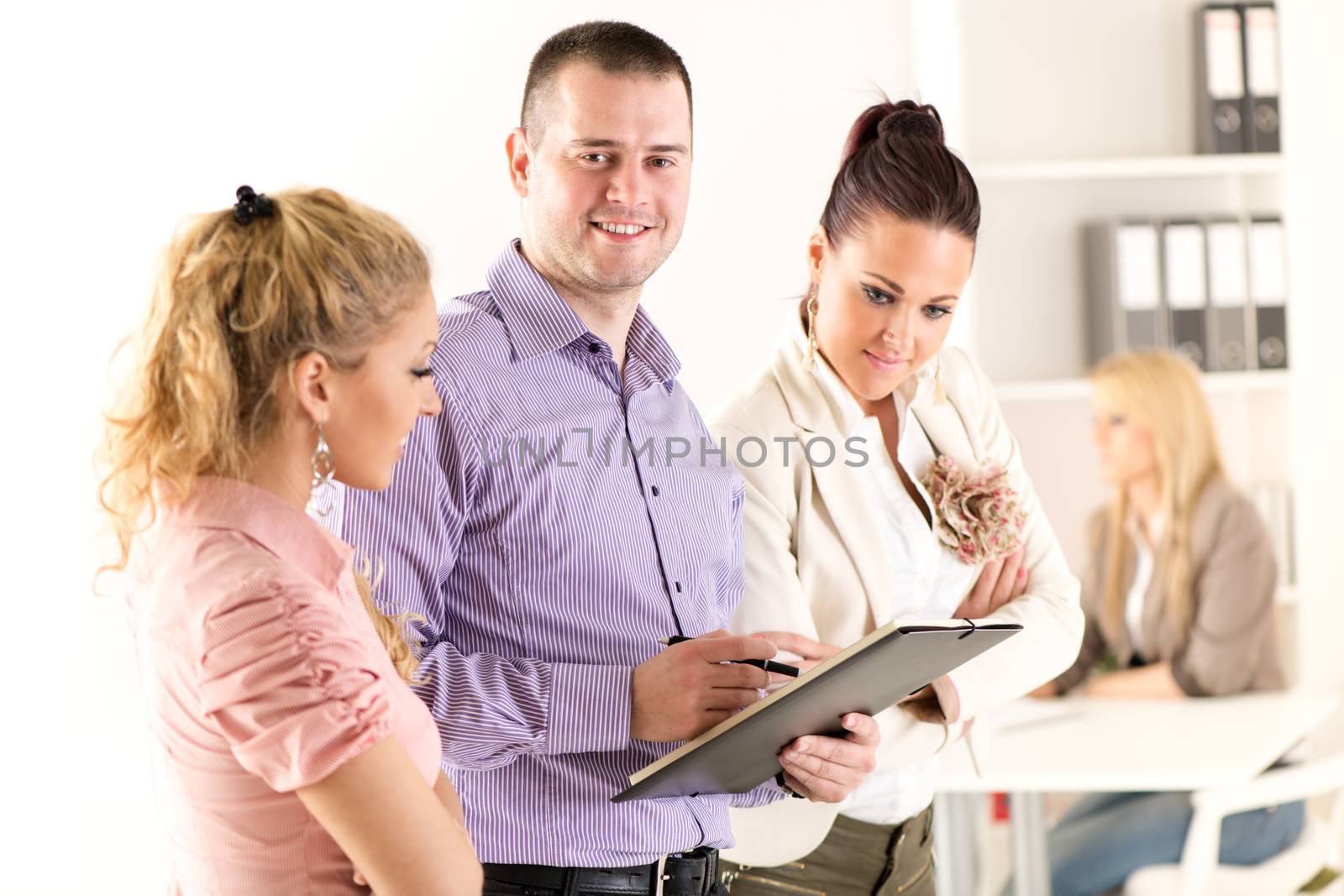 Three smiling co-workers standing in the office and discussing interesting question.