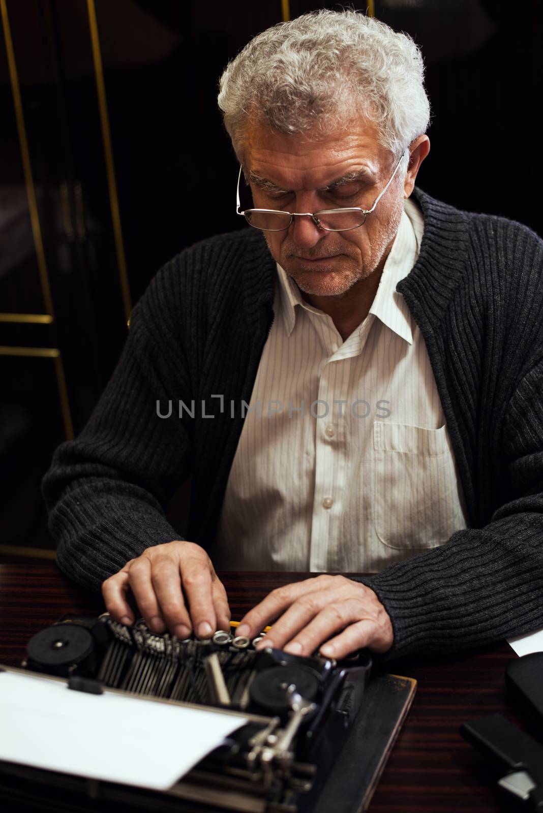 Retro Senior man writer with glasses writing on Obsolete Typewriter.