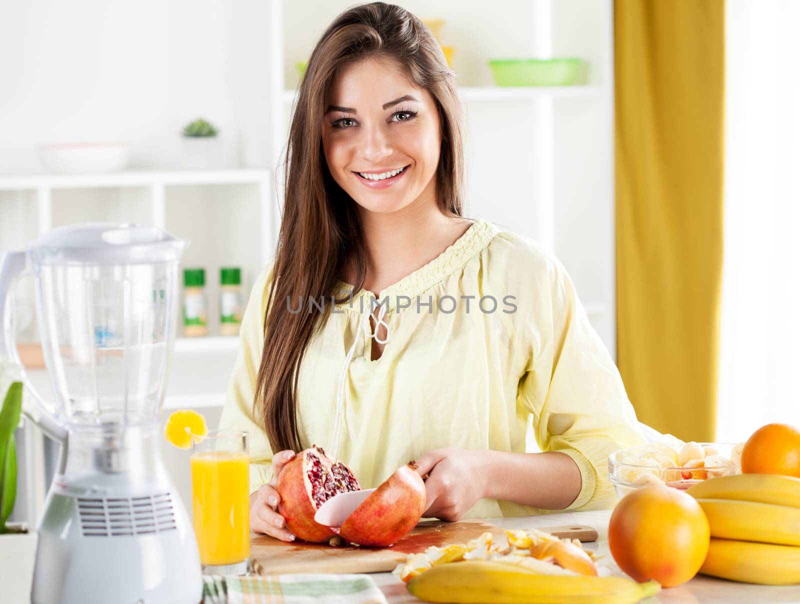 Beautiful young woman cutting pomegranate in the kitchen. Looking at camera and smilling.