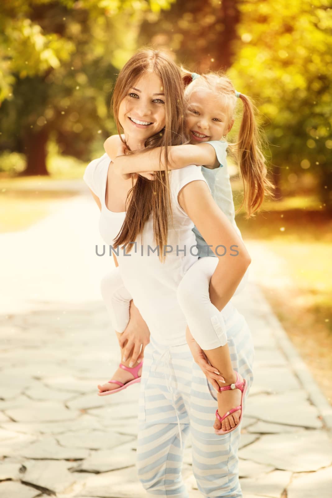 Beautiful mother and daughter having fun in the park on spring day. Young mother piggybacking his daughter.