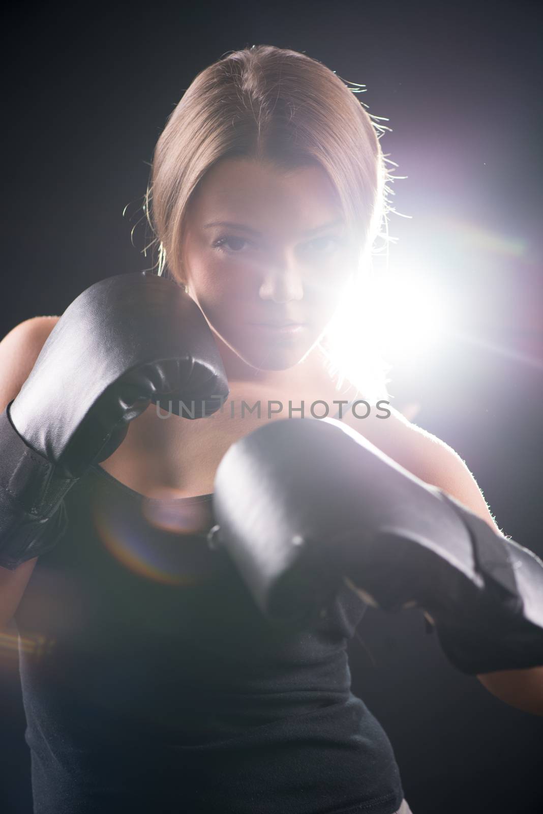 Portrait of Young beautiful boxing girl standing with a guard ready to punch. Black background with direct light.