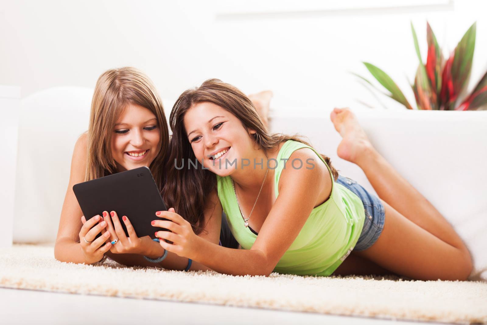 Two Beautiful teenage girls lying on the carpet and surfing internet on tablet pc