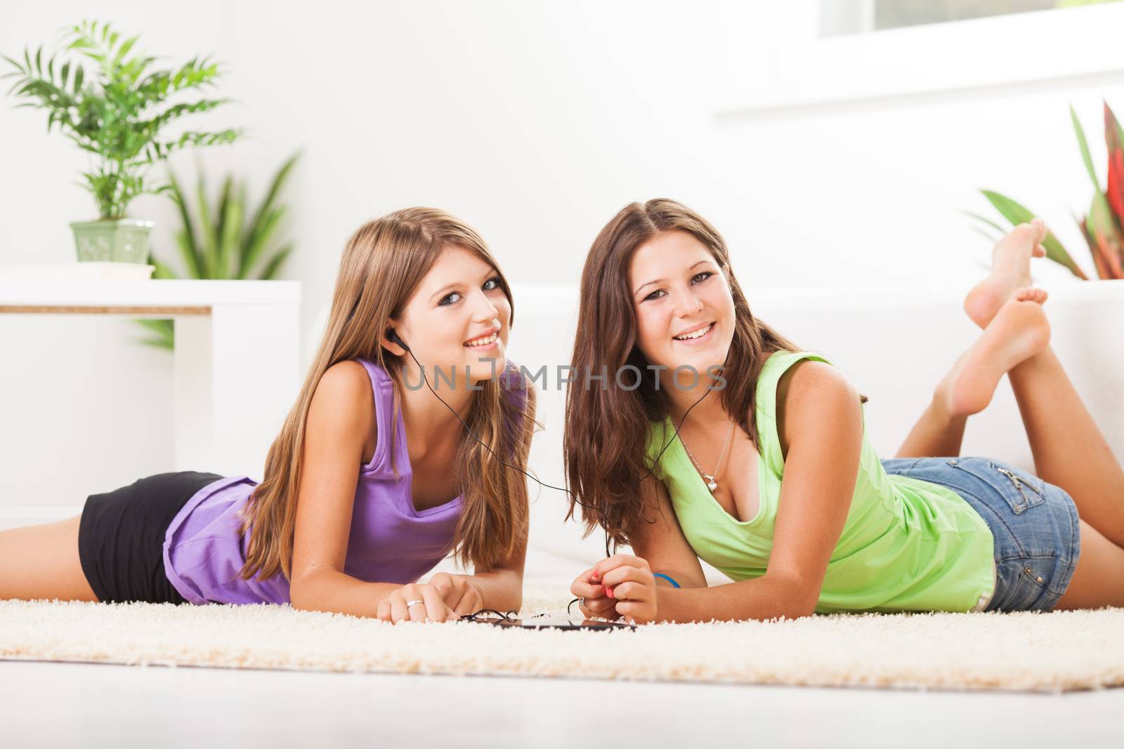 Two Beautiful teenage girls lying on the carpet and listening music from tablet pc