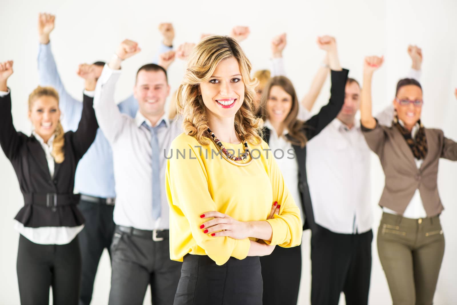 Successful and Smiling businesswoman with crossed arms standing in front of happy colleagues and looking at the camera.