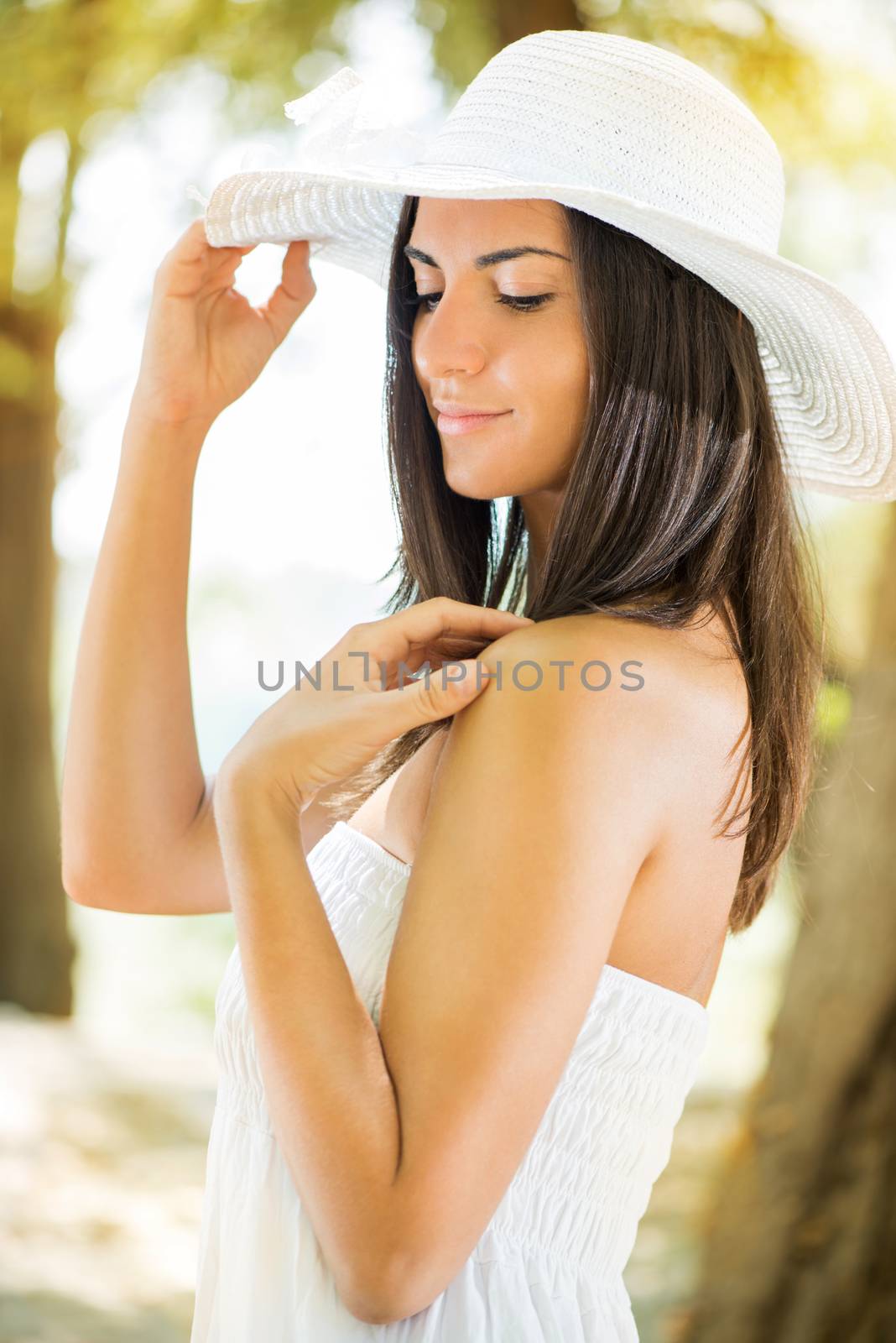 Portrait of young beautiful woman with white sun hat and white dress relaxing in the forest.