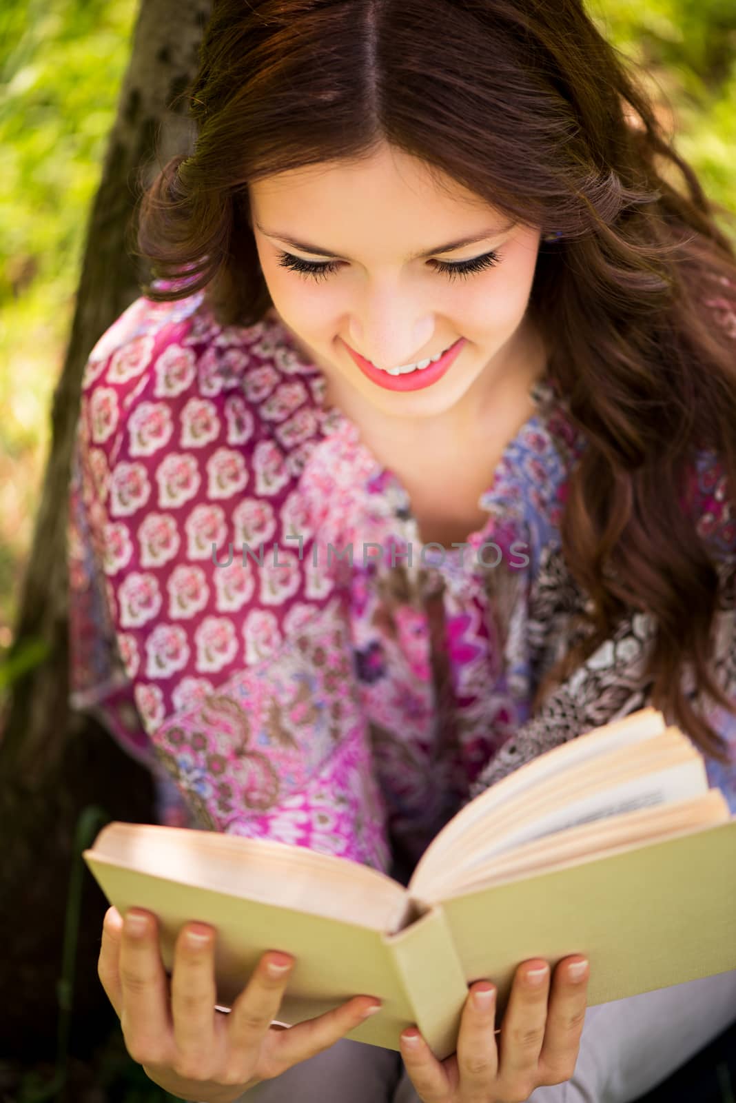 Beautiful Girl with a book in the park sitting on the grass and Expressing Positivity.