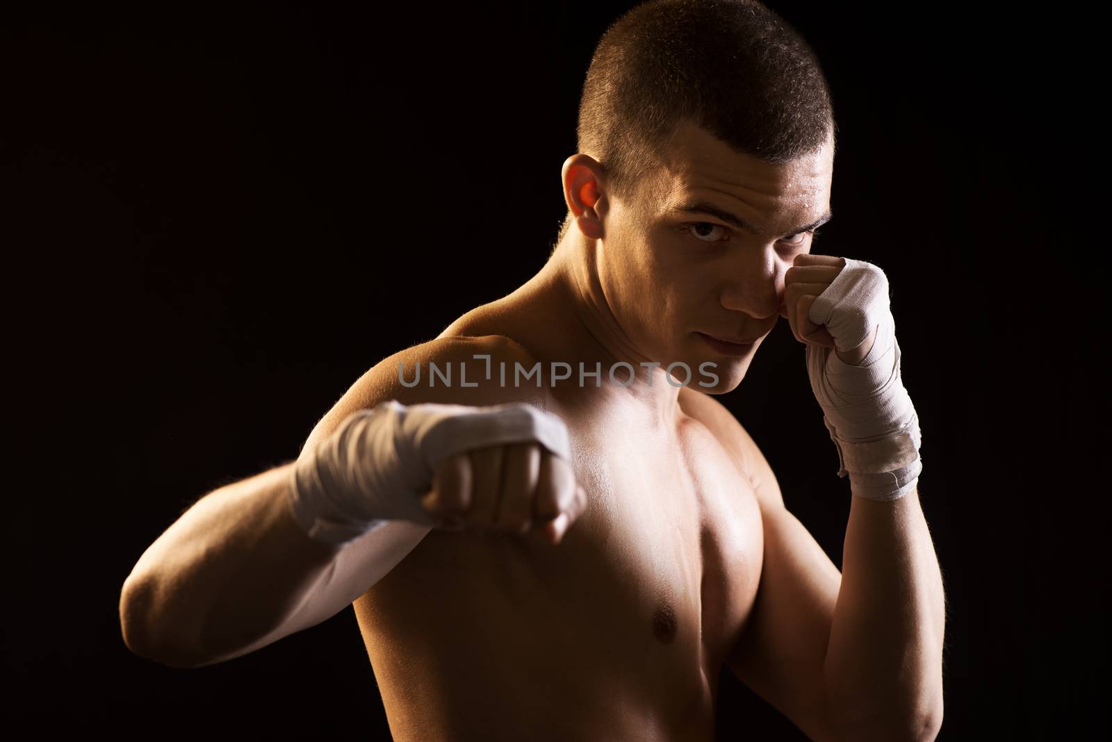 Young Fighter on black background in attack position. Only Boxing Straps on his hands.