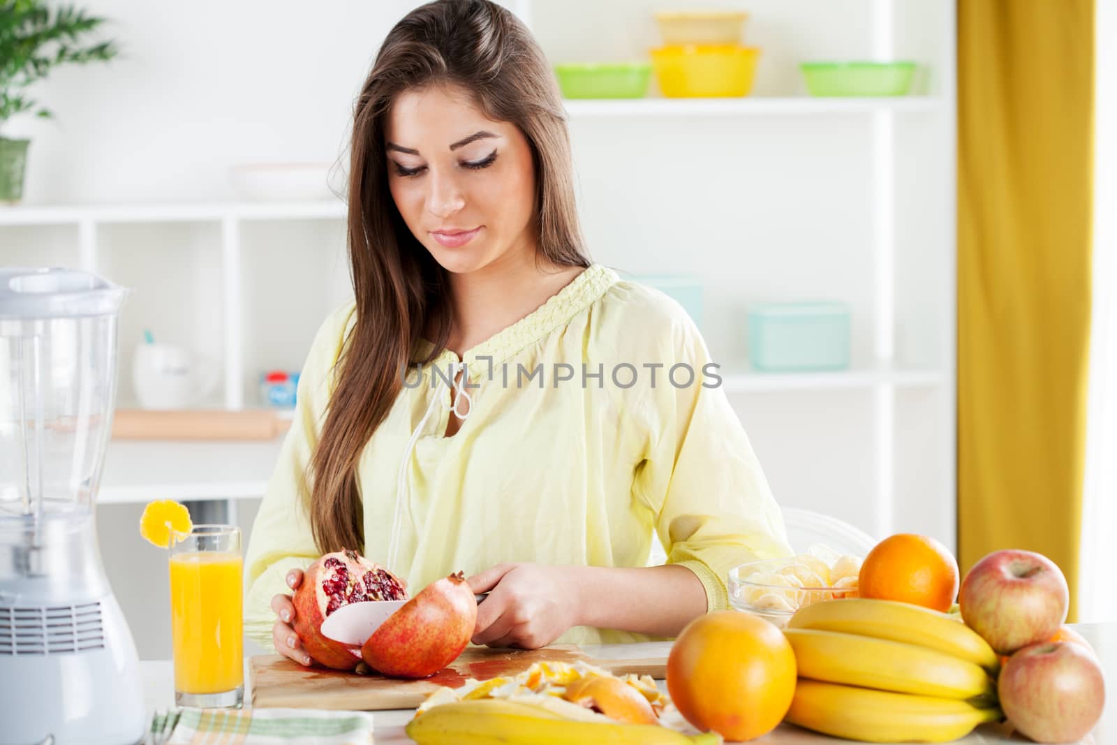 Beautiful young woman cutting pomegranate in the kitchen. 