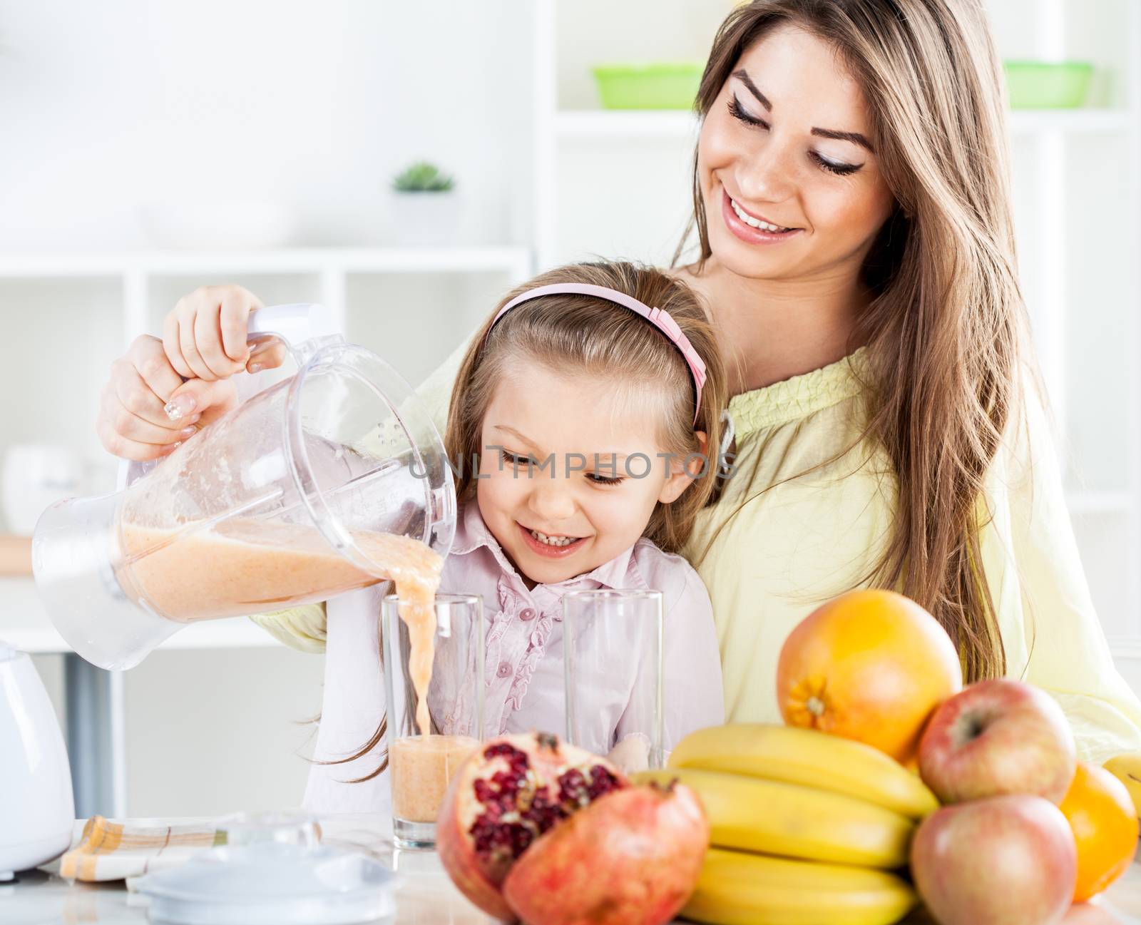 Beautiful young woman and cute little girl pouring juice from blender in the glass. In the kitchen concept.